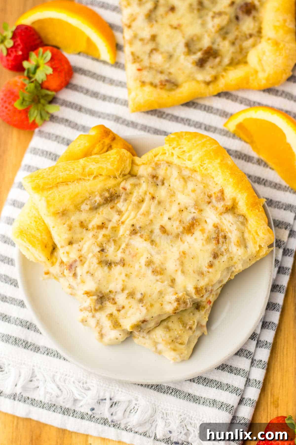A close-up shot of two slices of School Breakfast Pizza on a white plate, highlighting the delicious sausage and gravy topping.