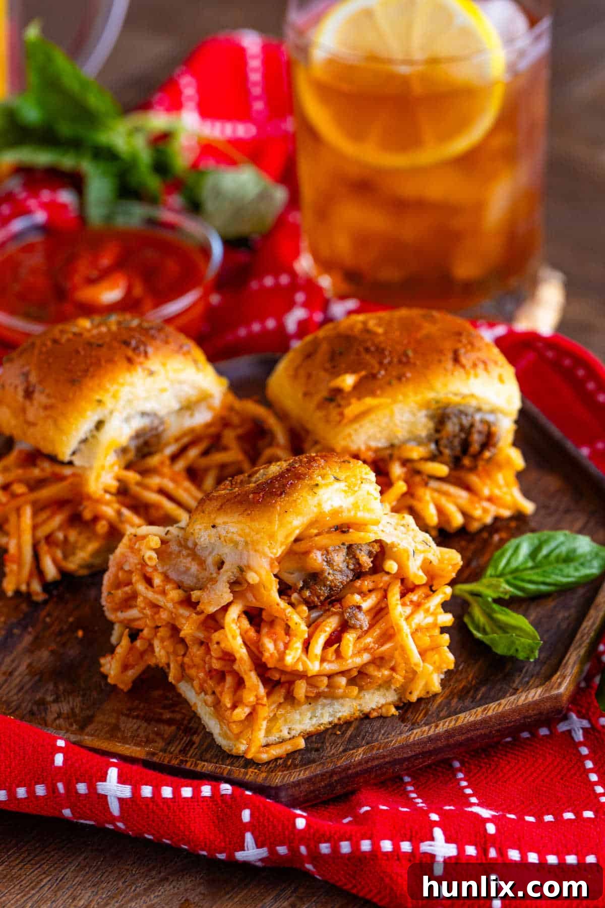 Freshly baked spaghetti and meatball sliders displayed on a wooden platter.