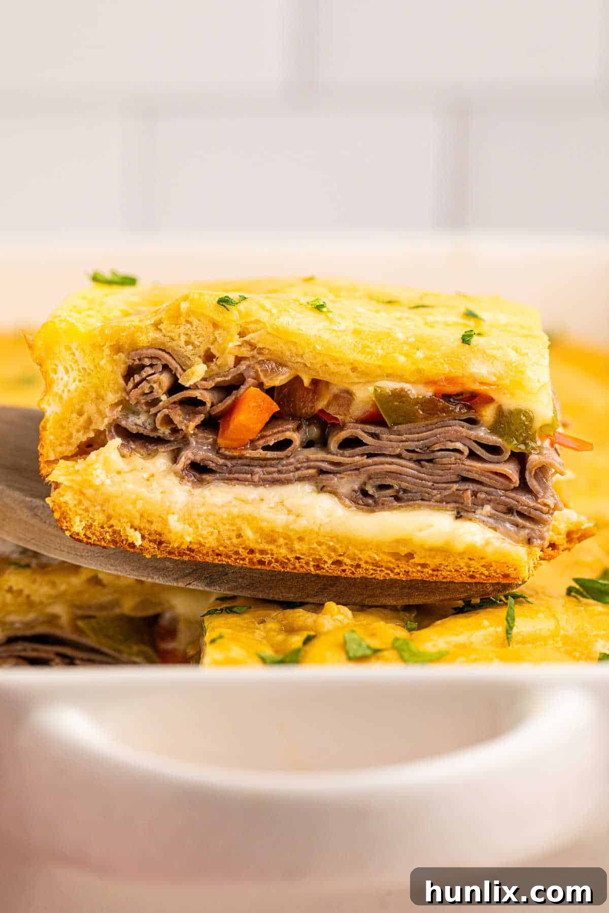 A golden-brown Philly cheesesteak square on a wooden spatula, showcasing the melted cheese and visible fillings.