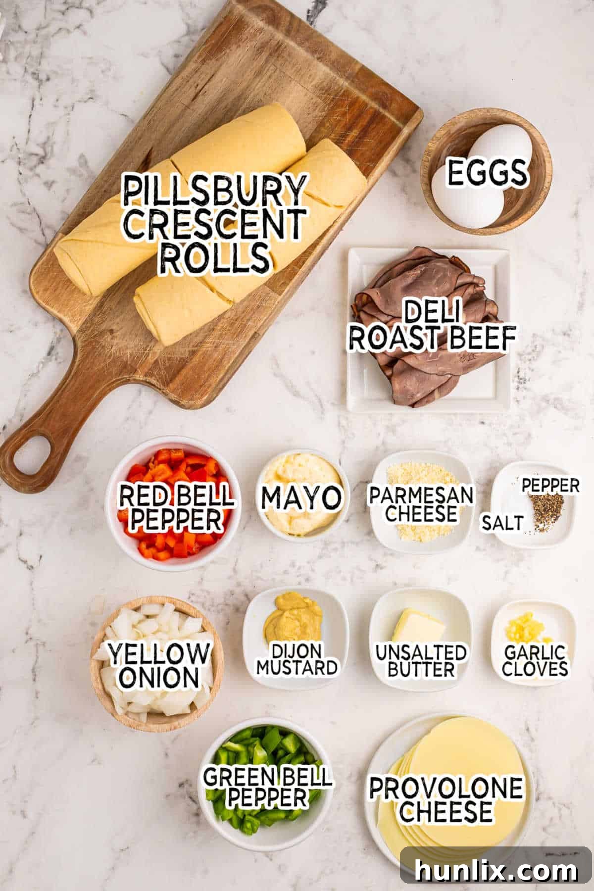 Various fresh ingredients laid out on a white surface, including bell peppers, onions, roast beef, crescent rolls, and cheese, ready for making Philly cheesesteak squares.