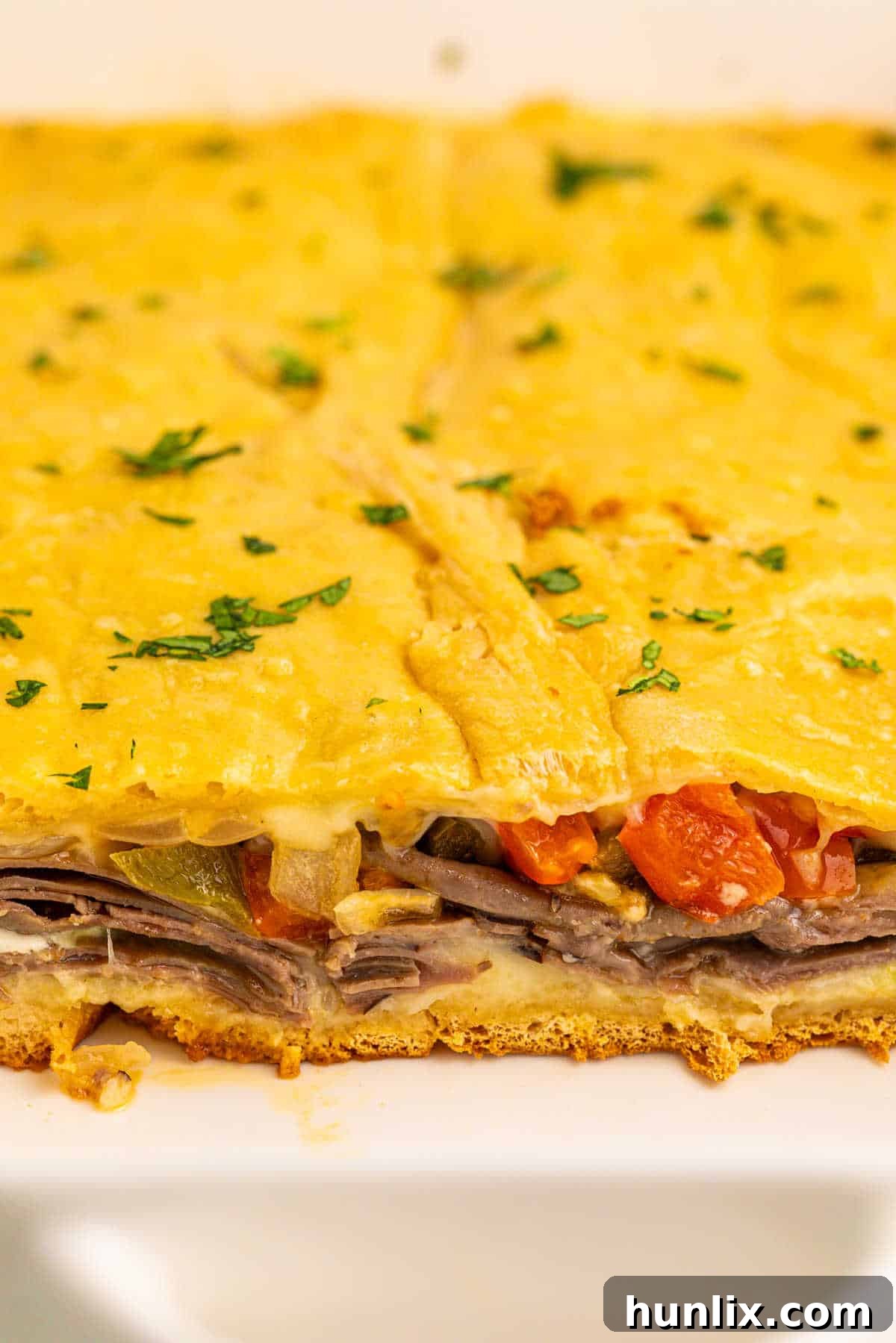 Baked Philly cheesesteak squares in a 9x13 inch baking pan, with several slices already cut and removed, showing the layers of filling.