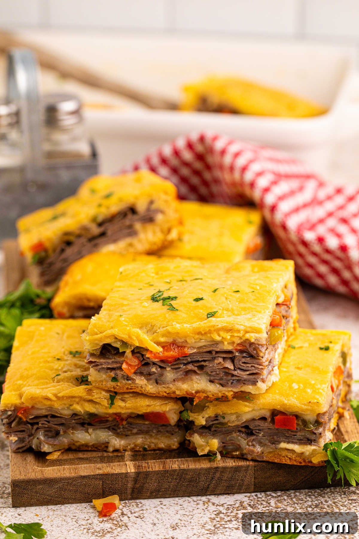 Multiple slices of Philly cheesesteak squares arranged on a wooden cutting board, ready for serving.