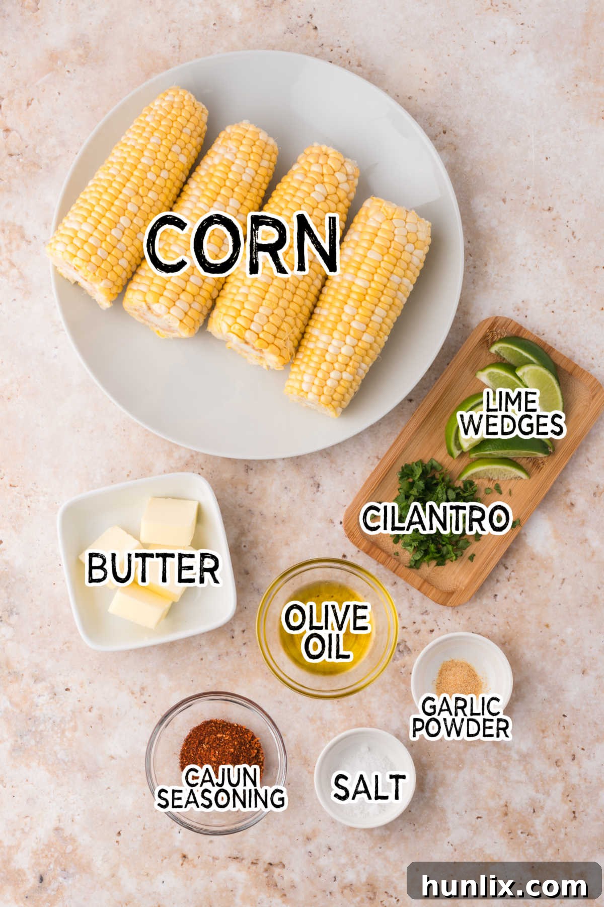 A selection of fresh corn on the cob and seasonings like olive oil, garlic powder, and Cajun spice on a beige background, ready for air frying.