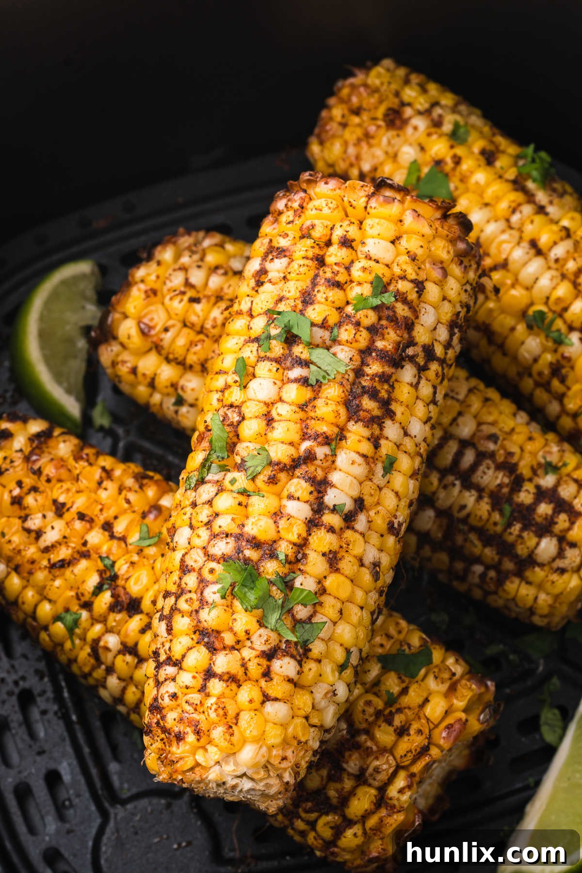 Multiple cobs of air fryer corn cooking in an air fryer basket, with some kernels showing a slight golden char.