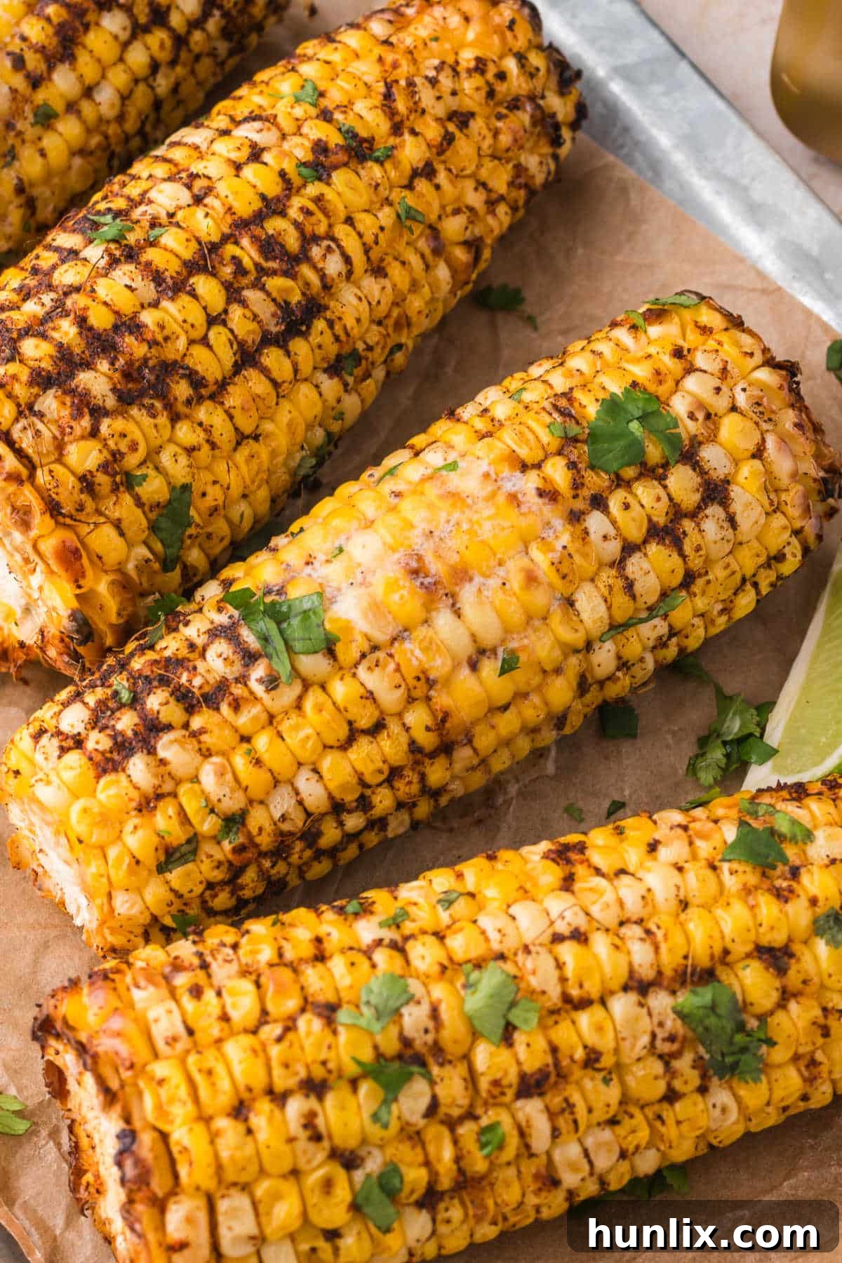 Three air fryer corn on the cob pieces, seasoned and cooked, resting on a sheet of parchment paper.