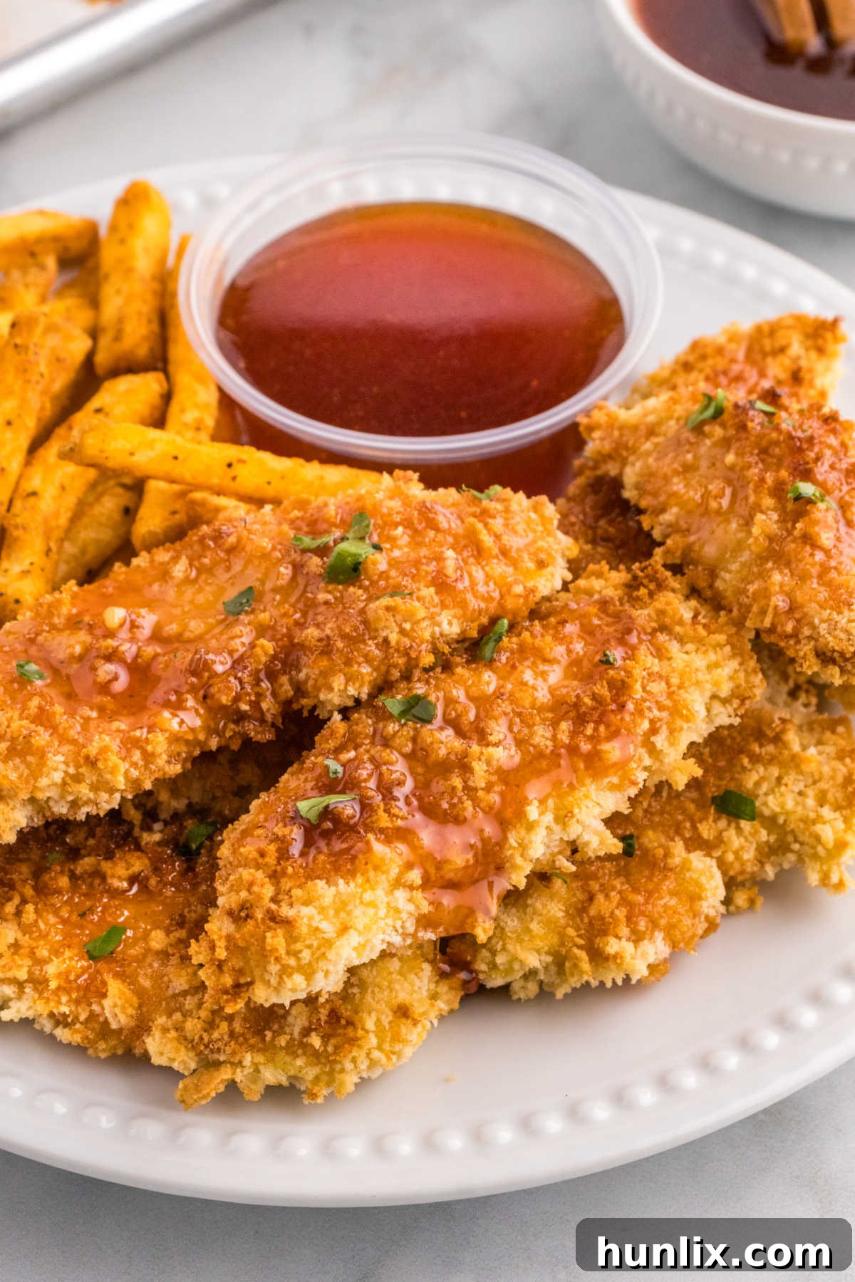 Hot honey chicken tenders on a plate with fries and hot honey sauce.