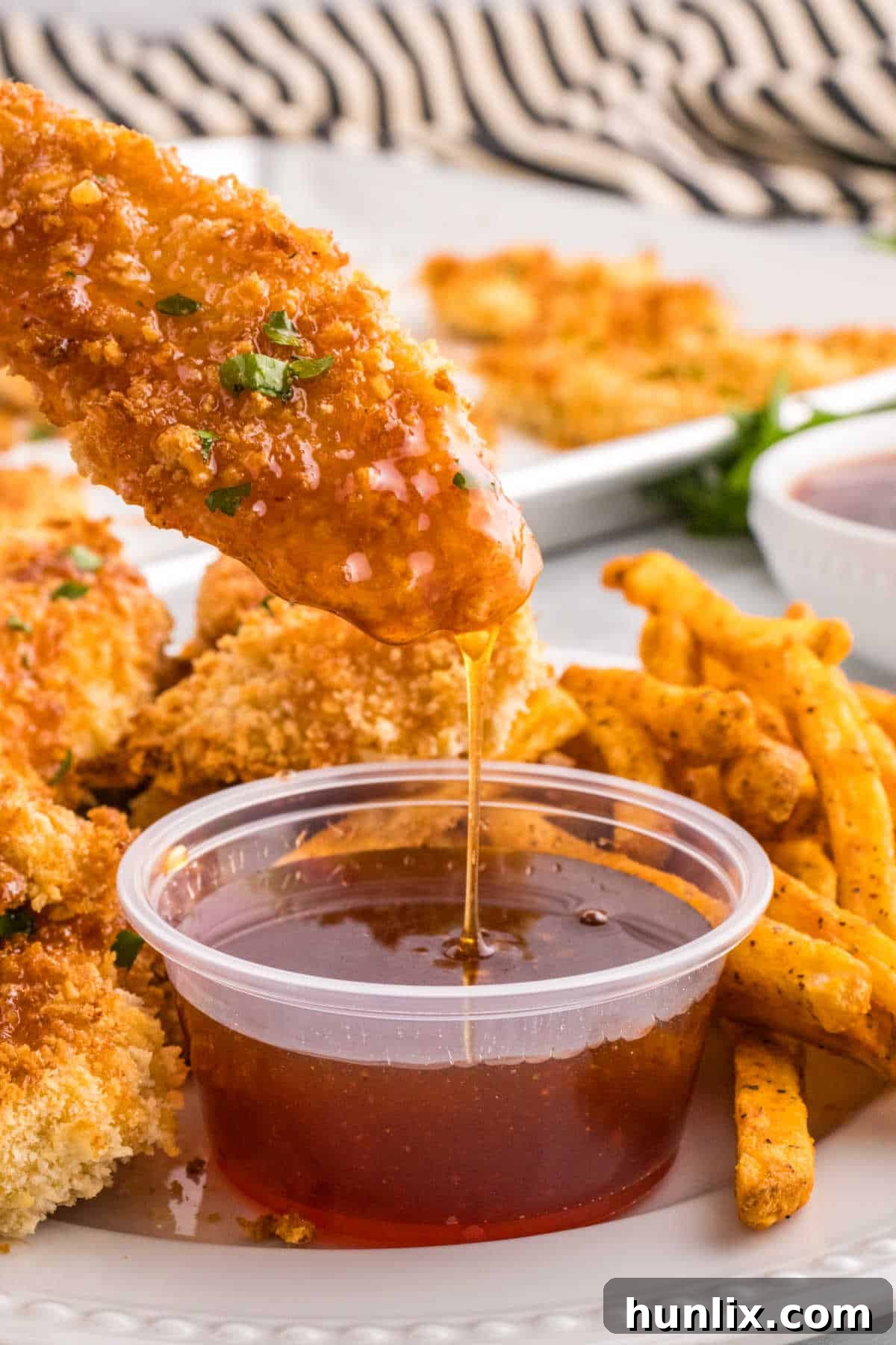 Hot honey chicken tenders being dipped in hot honey sauce.