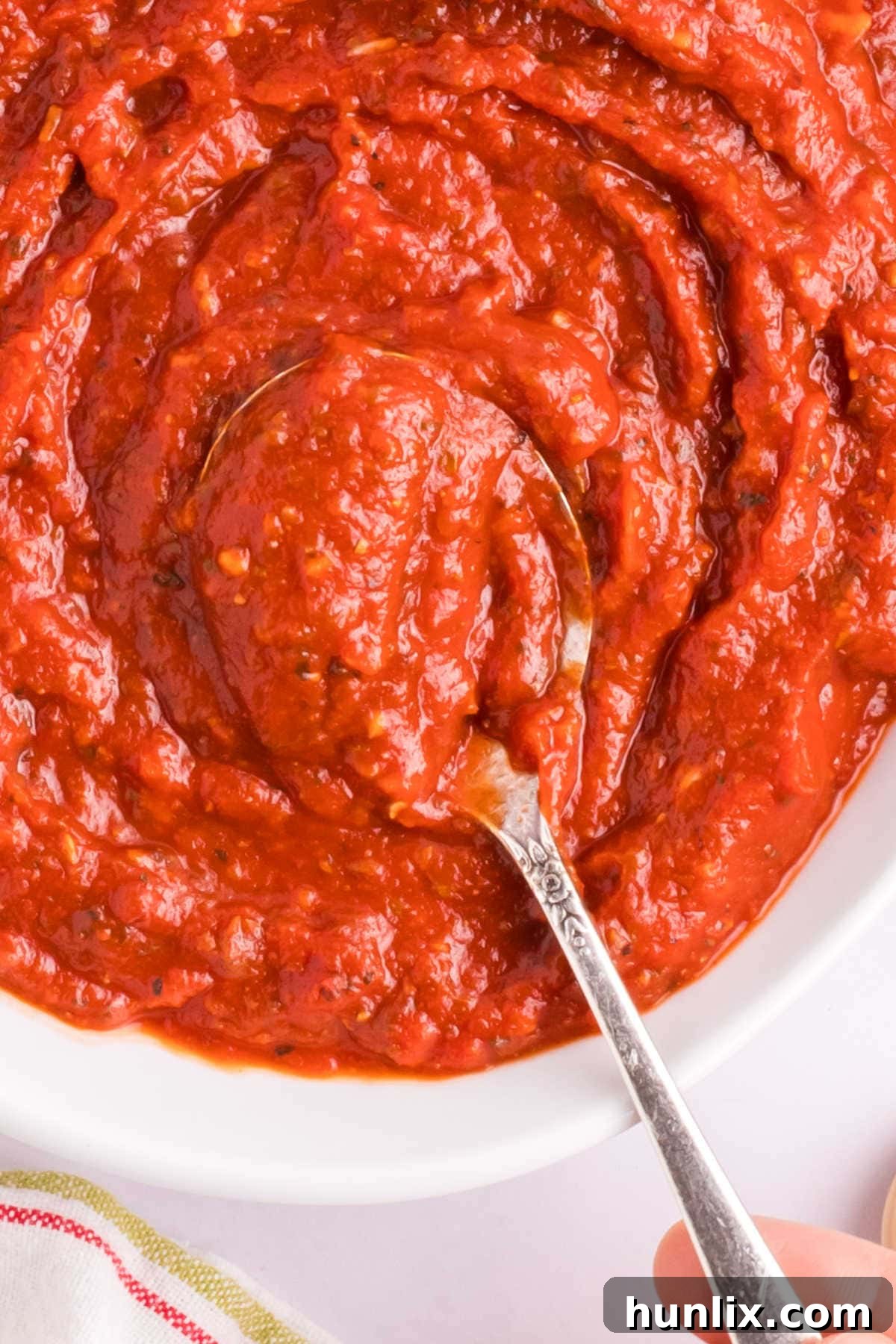 A bowl of homemade pizza sauce with a spoon, highlighting its inviting texture.