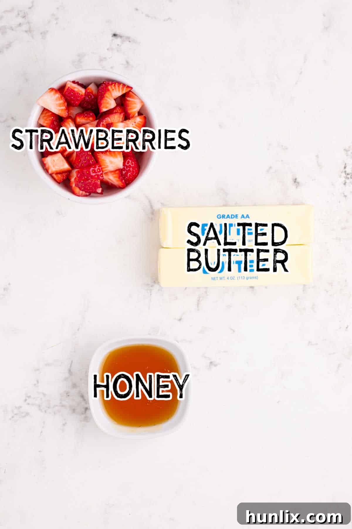 Whipped Strawberry Butter 3 Bir blok tereyağı, olgun çilekler ve bir kavanoz bal dahil olmak üzere taze malzemeler bir masanın üzerine serilmiş.