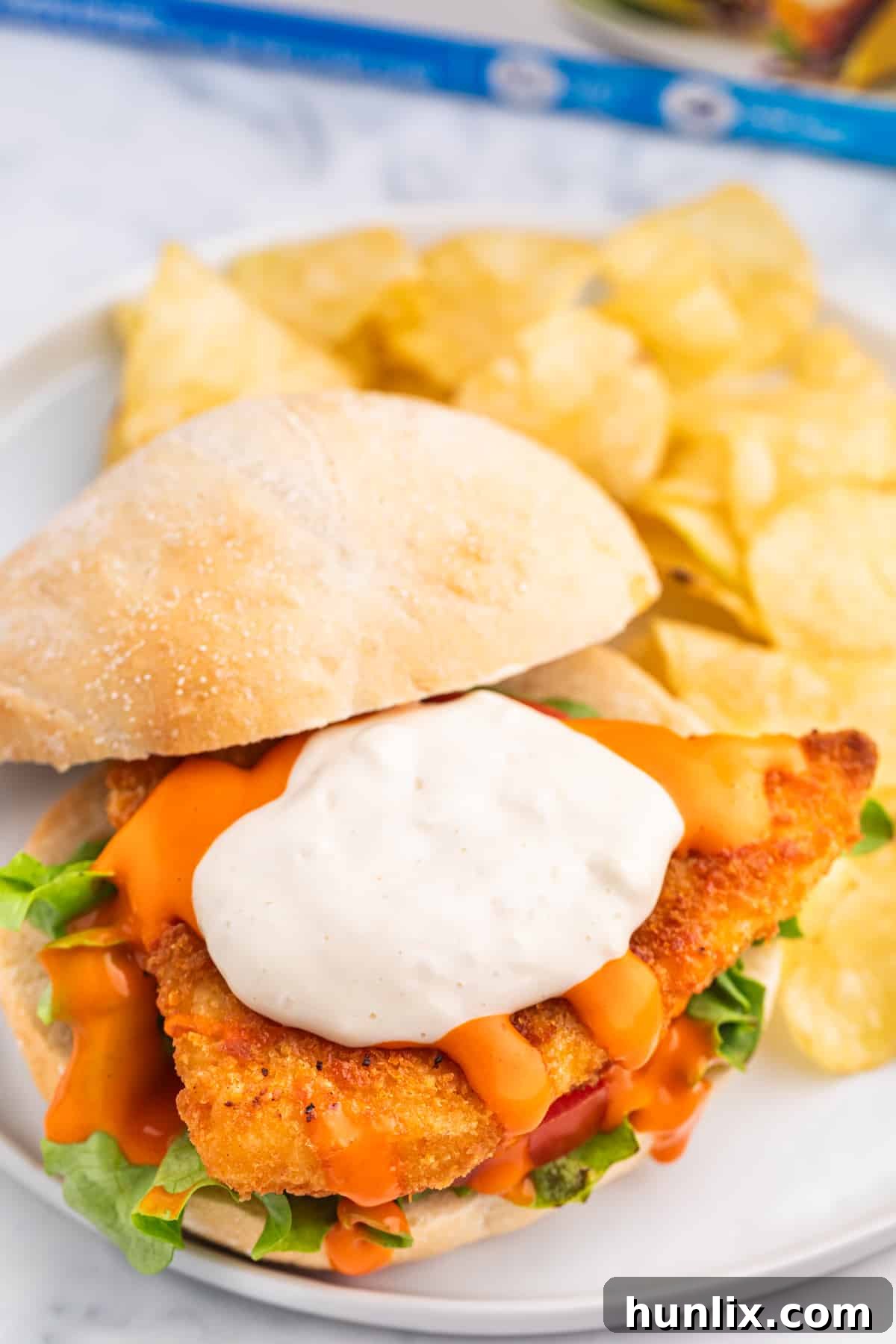 A buffalo cod filet sandwich on a plate with potato chips.