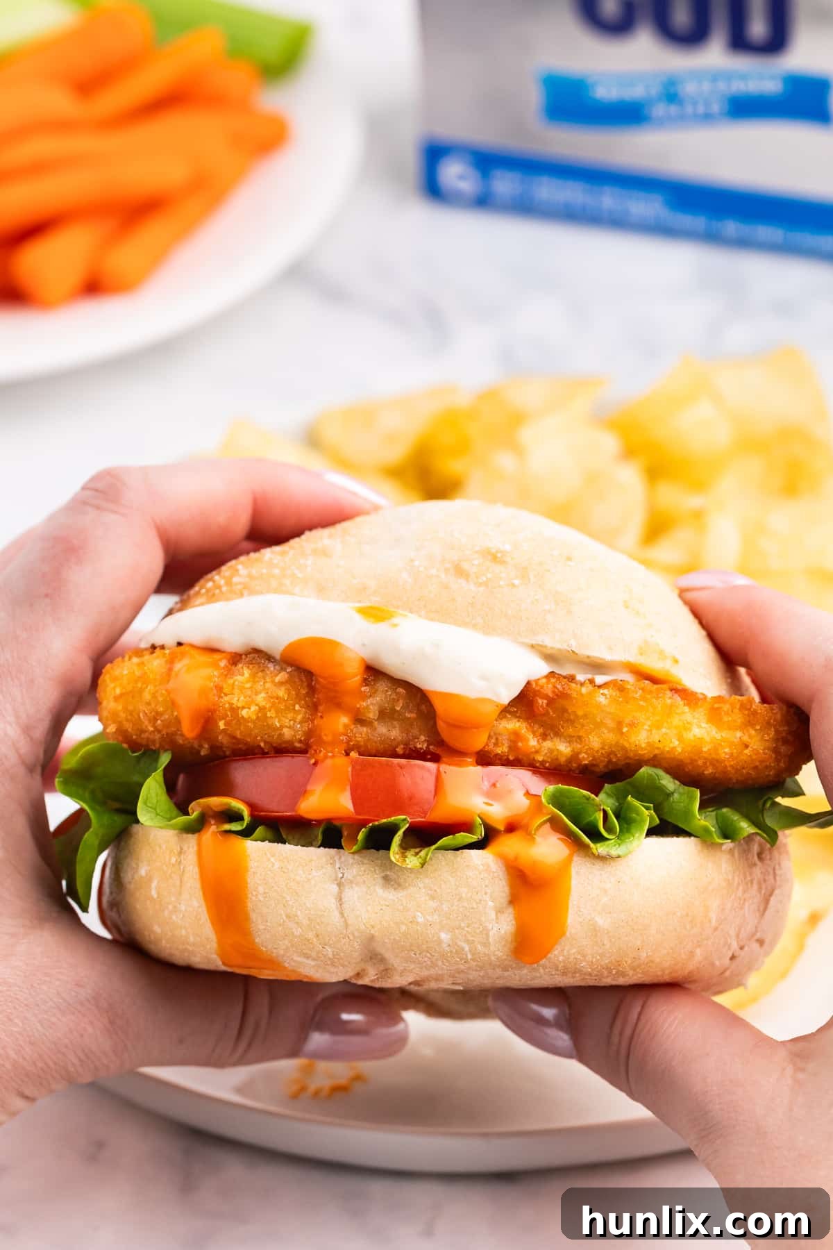 Hands holding a buffalo cod filet sandwich, showcasing its delicious layers.