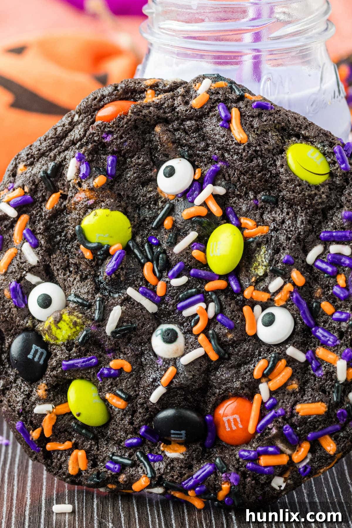 A cookie with a glass of purple milk behind it.