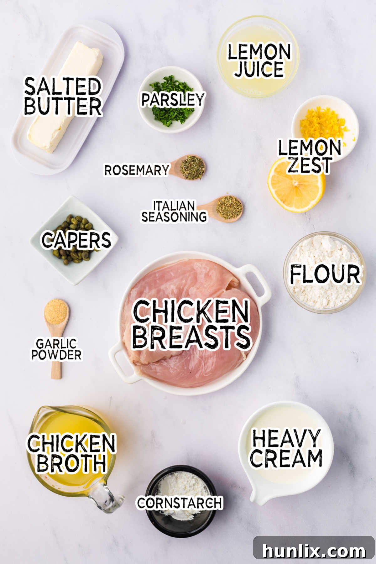 Various ingredients for lemon chicken piccata laid out on a white kitchen counter.