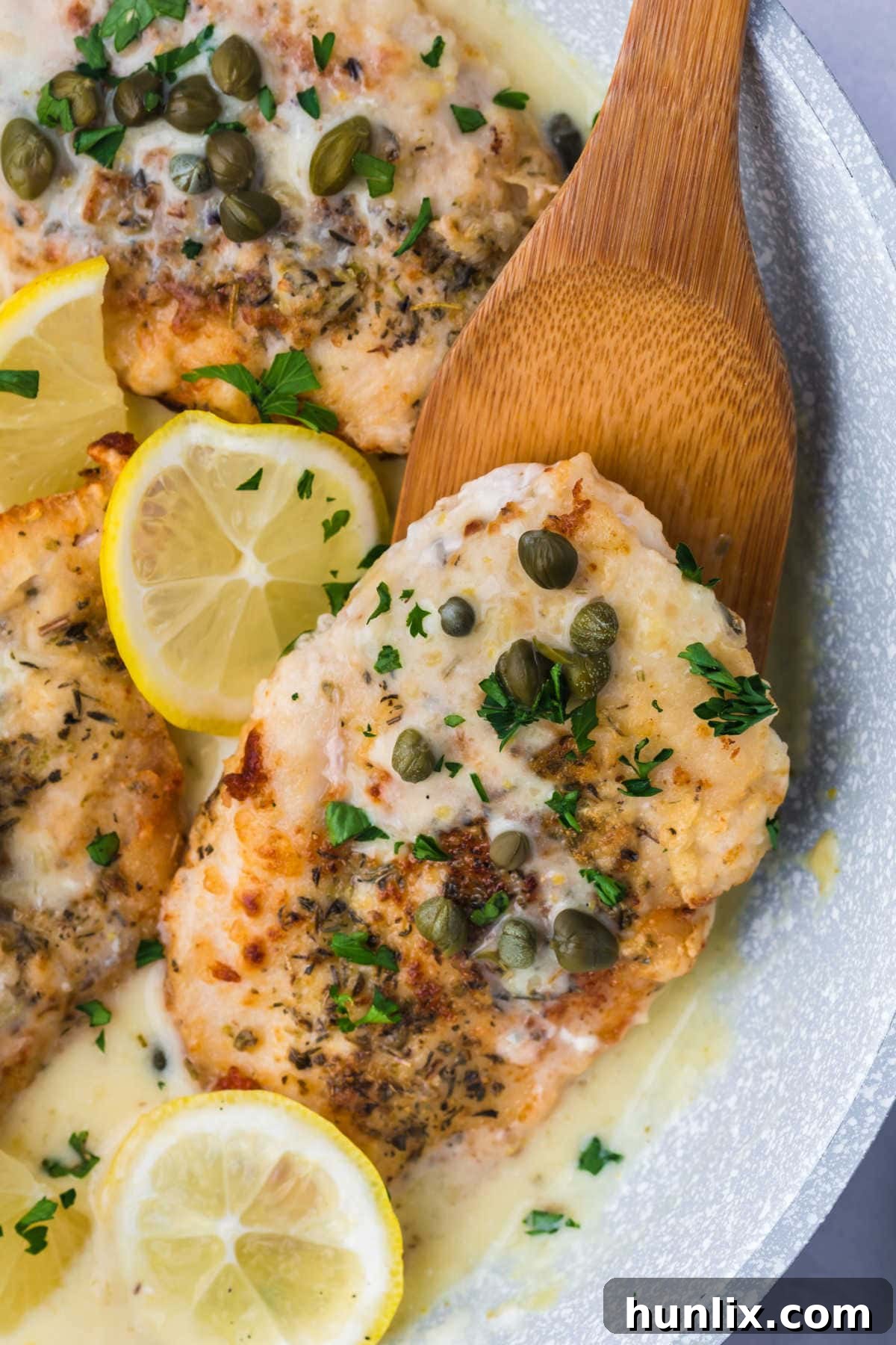 A golden-brown chicken breast being lifted from a pan with a wooden spoon.