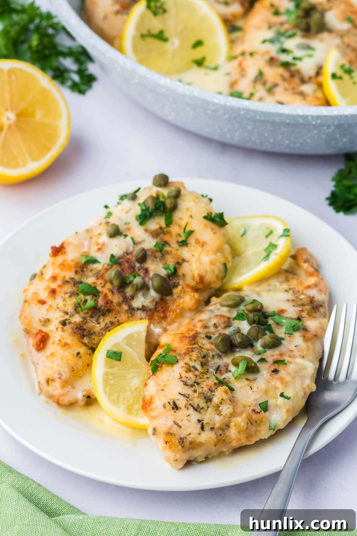 A slice of lemon chicken piccata on a plate with a fork.
