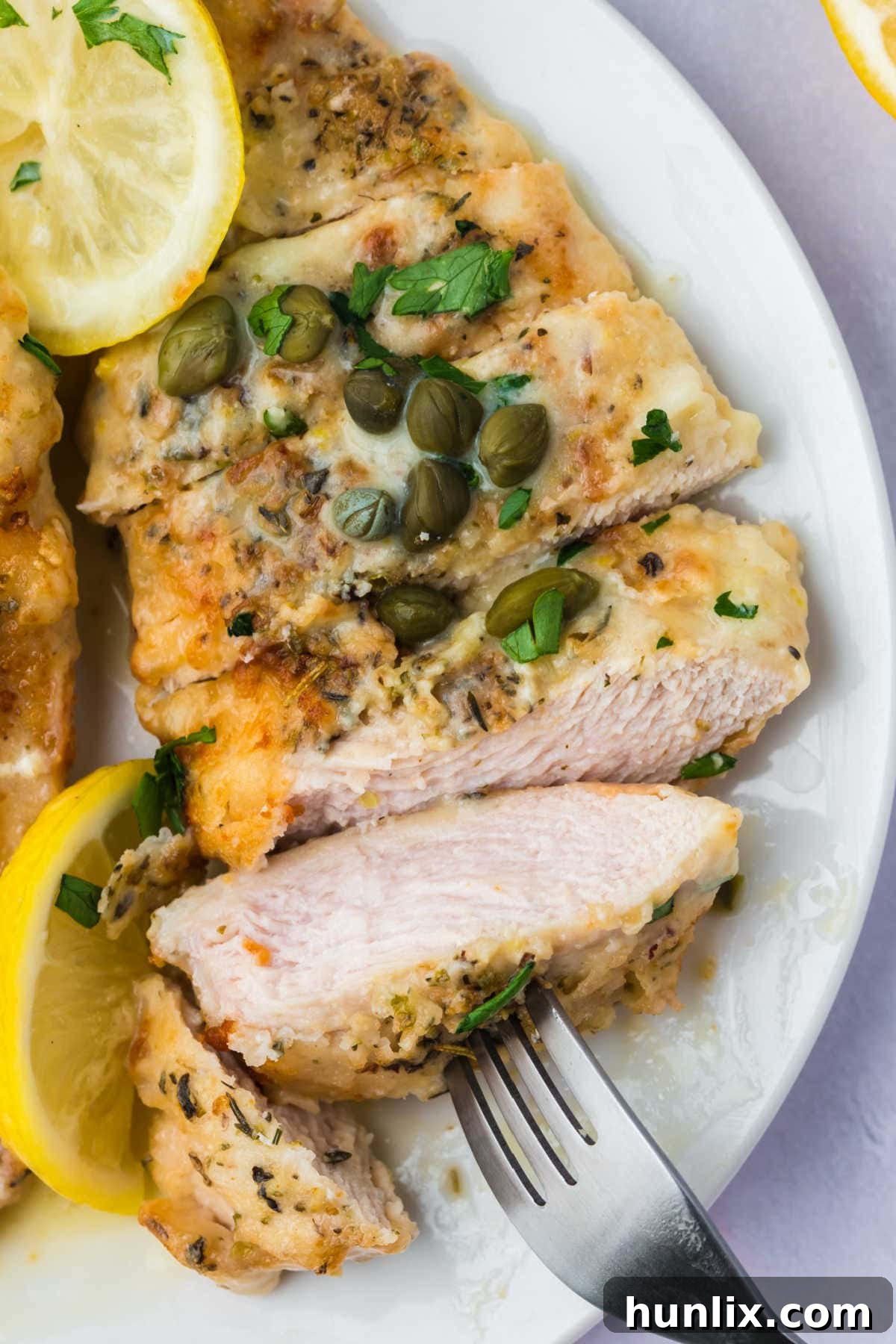 Sliced lemon chicken piccata on a white plate with a fork.