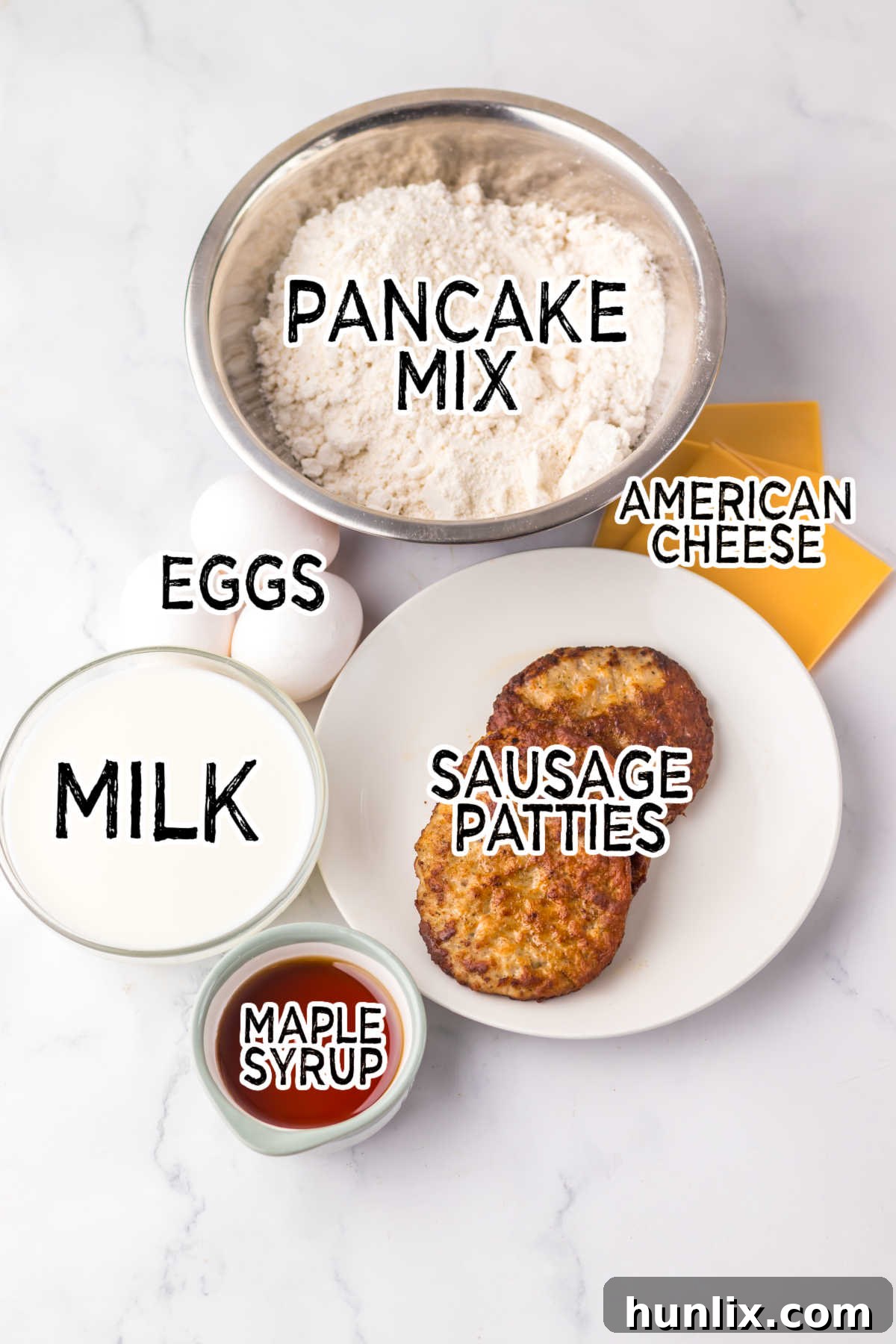 Various ingredients for making copycat McGriddles laid out on a white kitchen counter, including pancake mix, maple syrup, eggs, sausage patties, and American cheese slices.