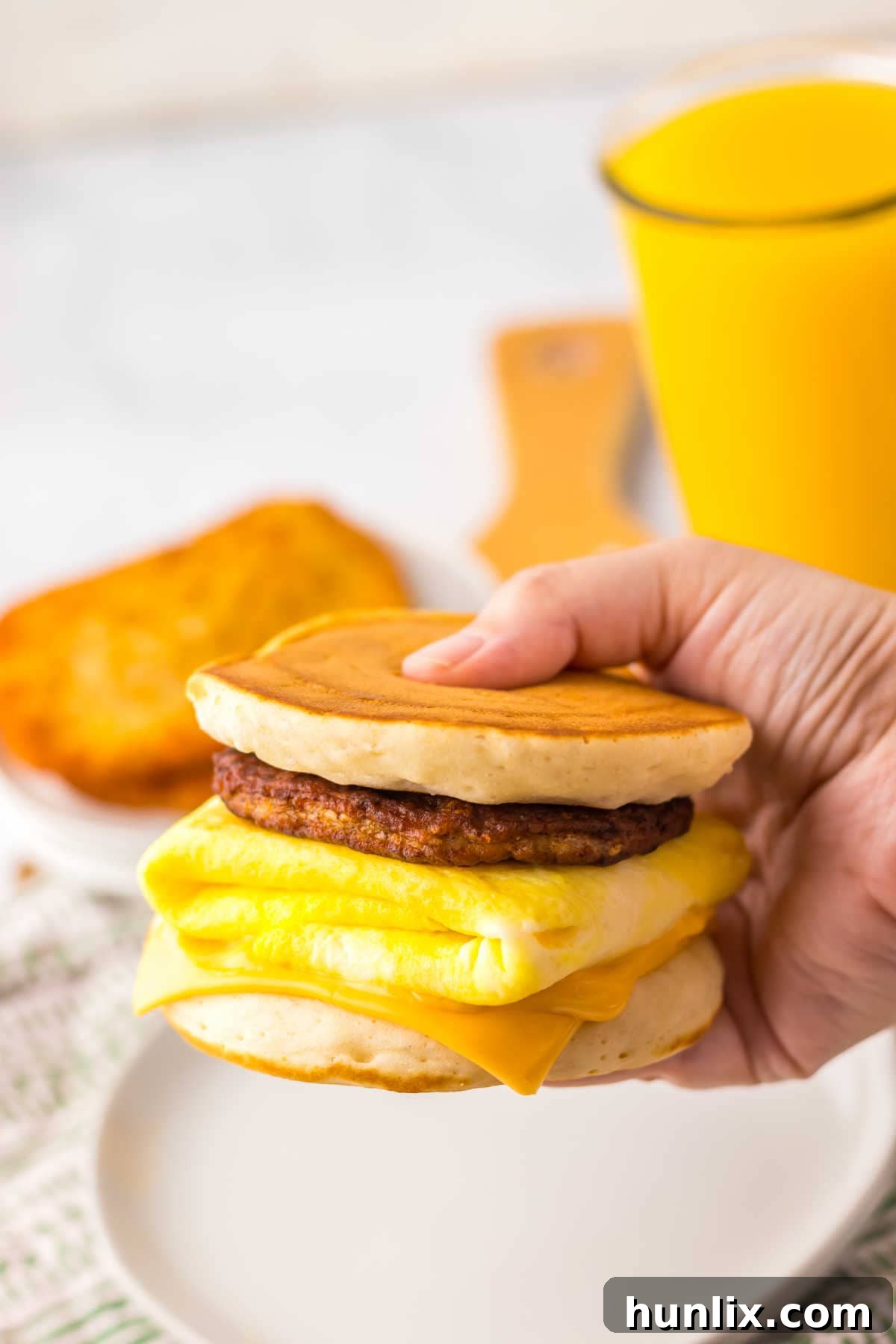 A hand holding a perfectly assembled copycat McDonald's McGriddle, showcasing the layers of maple pancake, cheese, egg, and sausage.