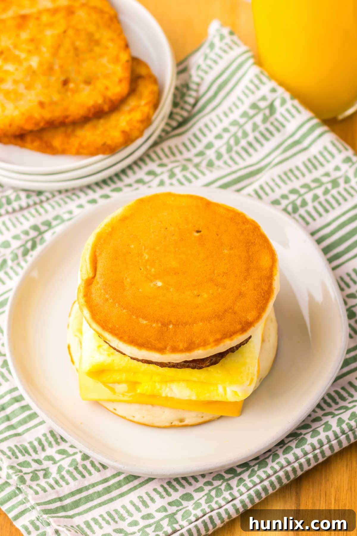 A close-up shot of a freshly assembled copycat McDonald's McGriddle, cut in half to show the layers of maple pancake, melted American cheese, fluffy egg, and savory sausage.