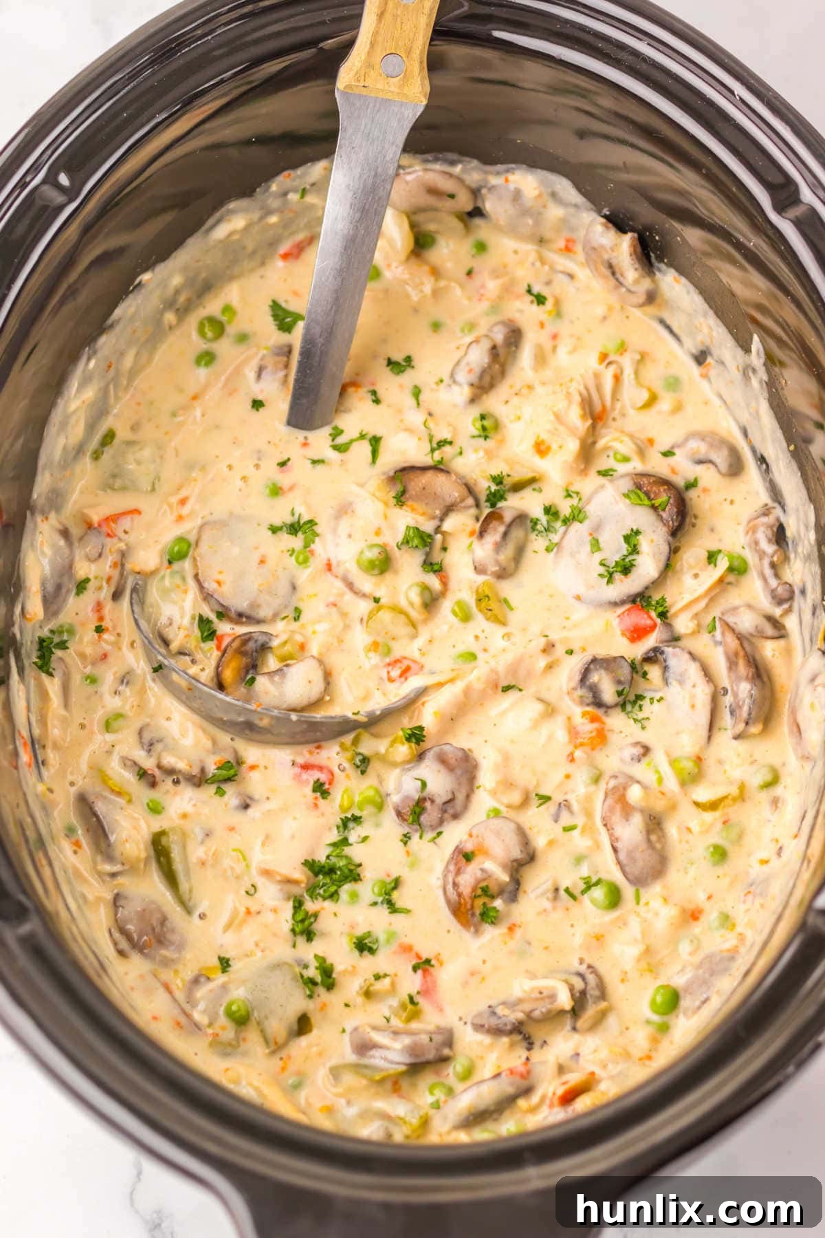 Effortless Slow Cooker Turkey a la King 2 Slow cooker turkey a la king in a black Crockpot with a ladle.