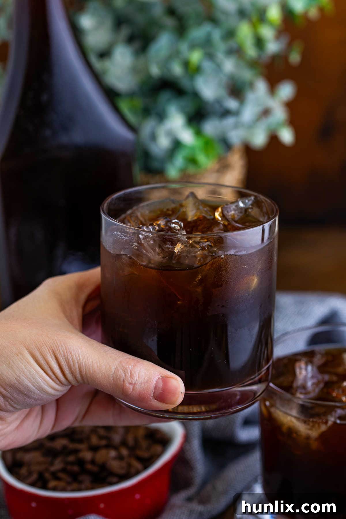 Craft Your Own Coffee Liqueur 8 A hand holding a glass of homemade Kahlua, ready for a sip, against a blurred background.