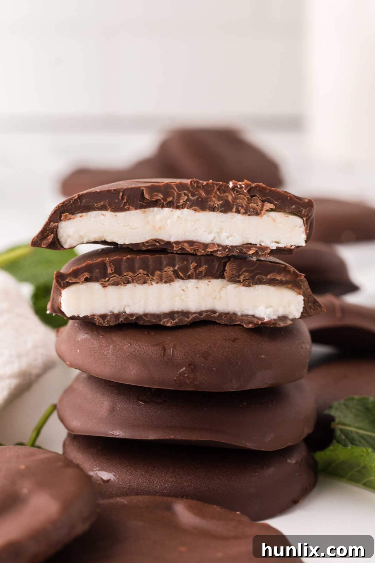 Artisan Peppermint Gems 2 A stack of homemade peppermint patties, with the top two cut in half revealing the creamy, vibrant mint center contrasted by the dark chocolate coating.