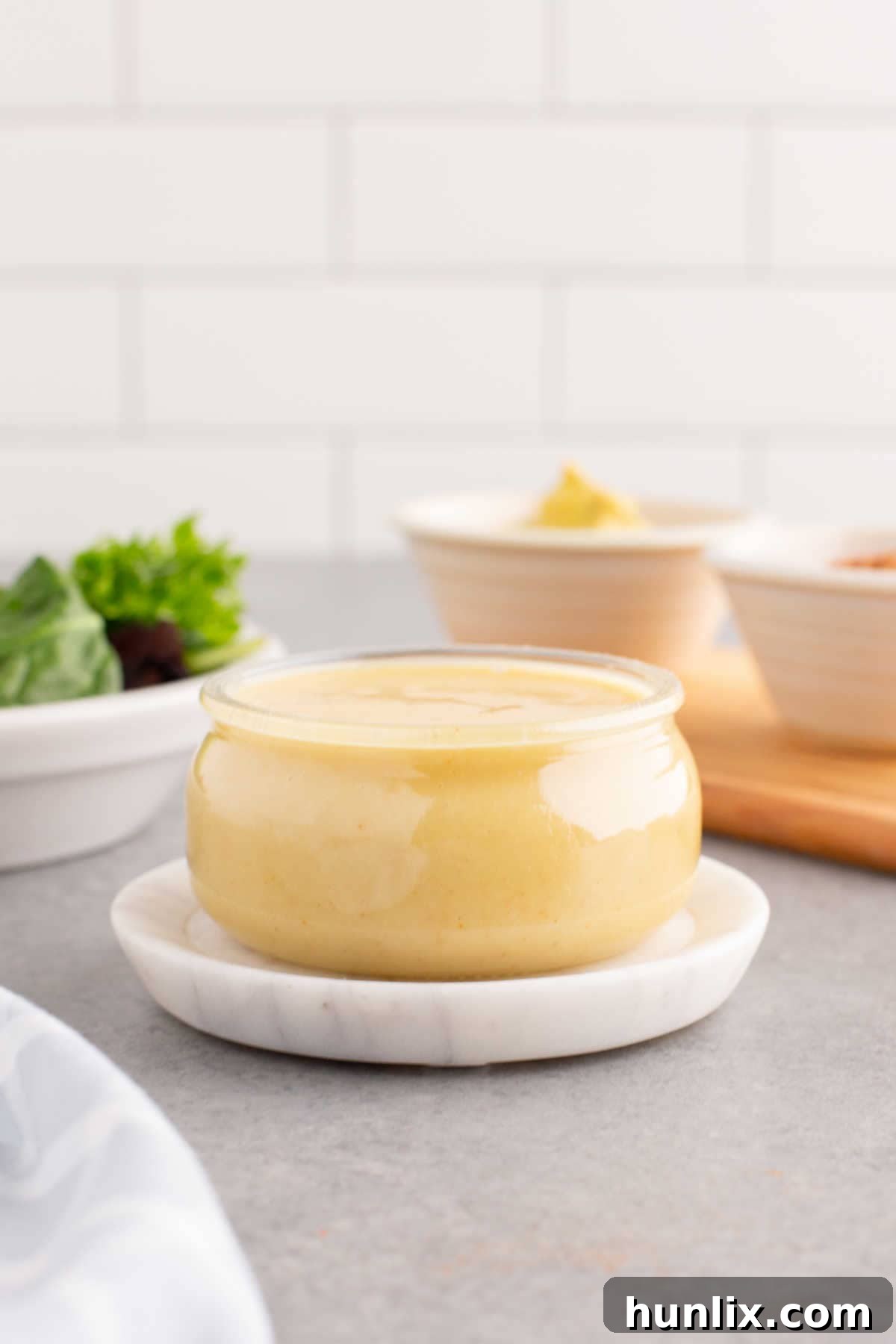Golden Honey Mustard 5 A clear glass jar filled with golden, creamy honey mustard sauce, set against a rustic background, highlighting its homemade appeal.