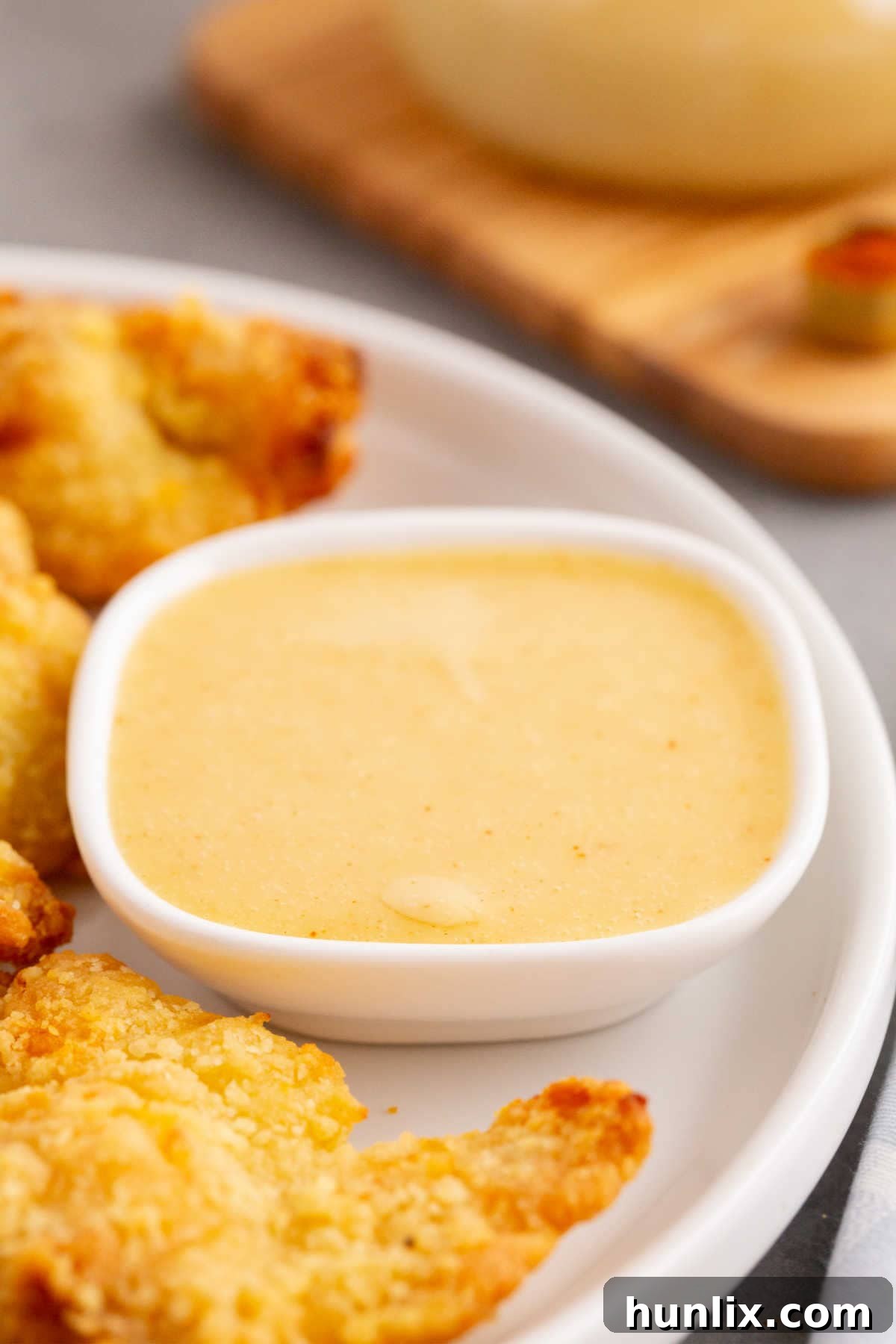 Golden Honey Mustard 6 A small bowl of creamy honey mustard sauce on a plate, surrounded by crispy chicken fingers, illustrating a perfect meal pairing.