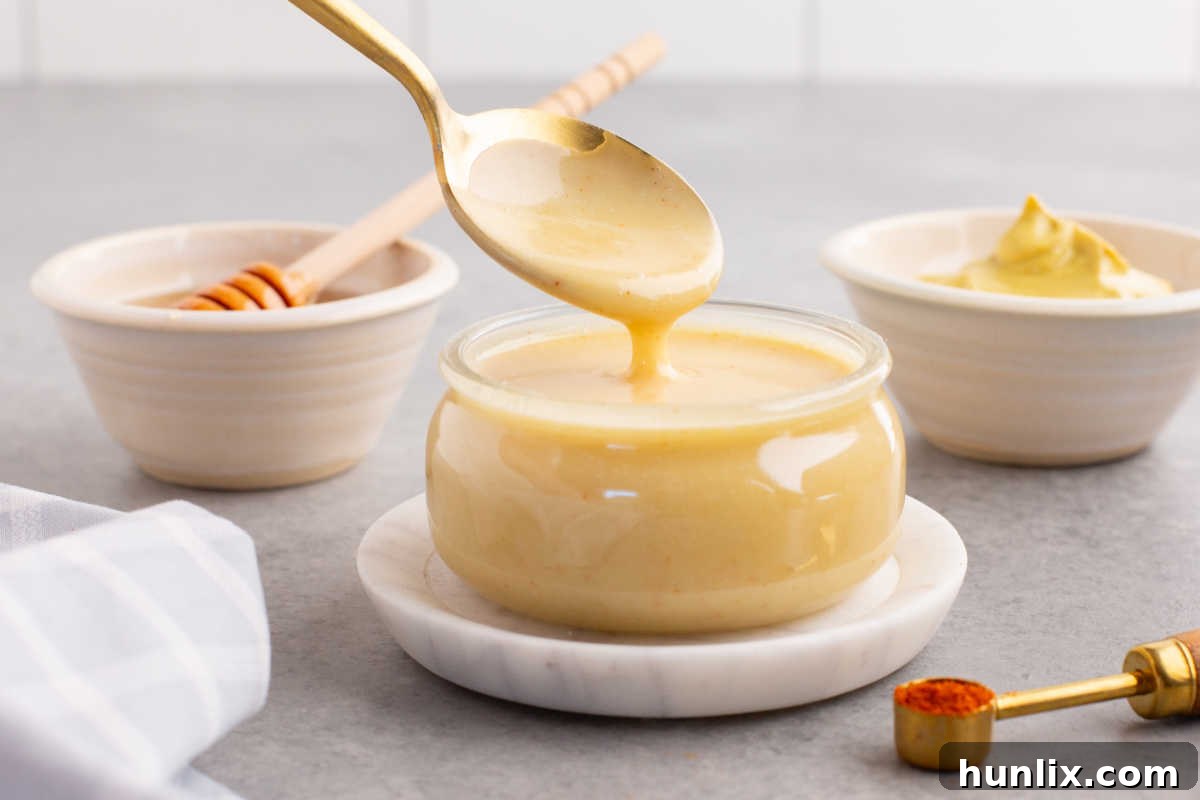 Golden Honey Mustard 7 A spoon drizzling thick, golden honey mustard sauce into a clear glass jar, emphasizing its creamy texture.