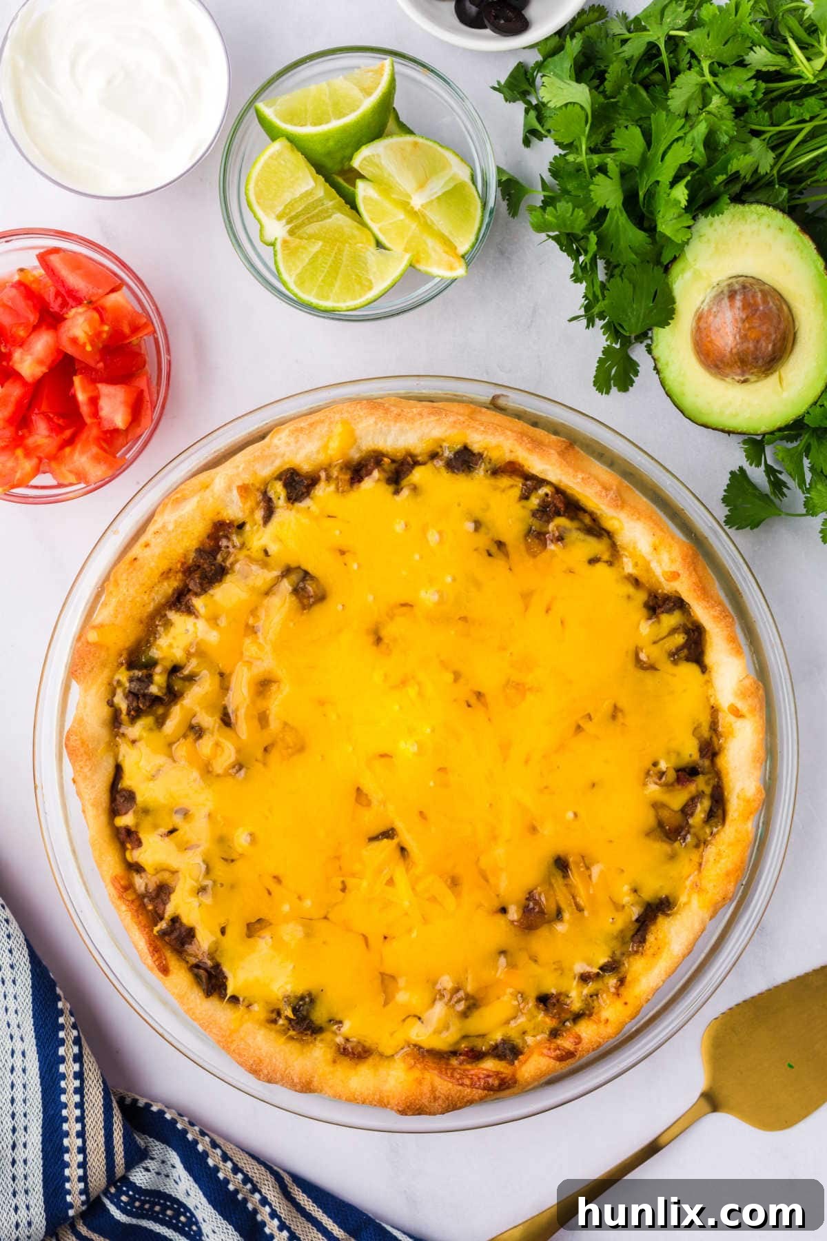 A perfectly baked Taco Pie surrounded by fresh ingredients like sour cream, cilantro, limes, and diced tomatoes, ready for serving.
