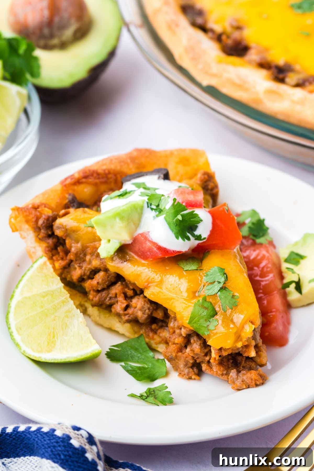 A generous slice of Taco Pie artfully presented on a plate, topped with fresh avocado, cilantro, and a dollop of sour cream.