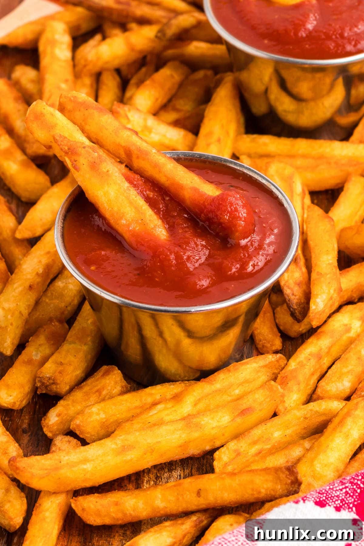 Two fries in a container of homemade ketchup and surrounded by more fries.