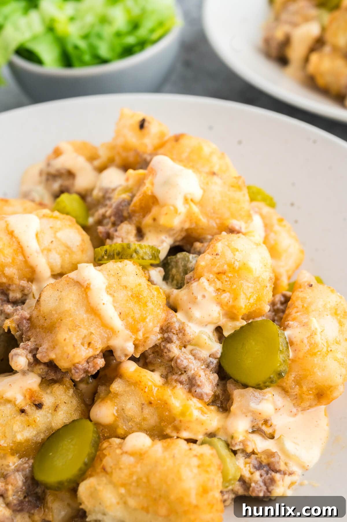 Loaded Big Mac Tater Tot Casserole 10 A serving of Big Mac Tater Tot Casserole on a white plate, topped with sauce and fresh garnishes.