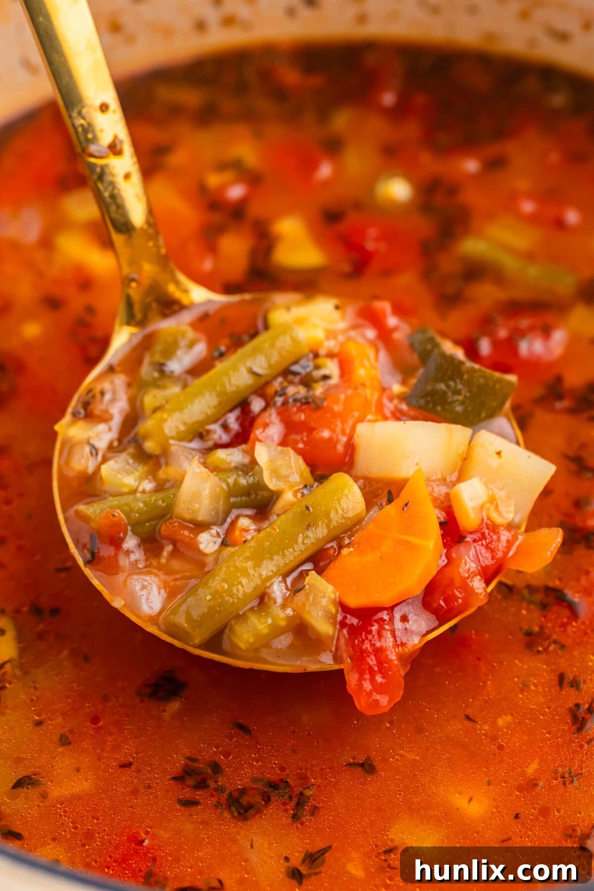 A ladle scooping a generous portion of steaming vegetable soup from a large pot, showcasing the colorful array of fresh vegetables.