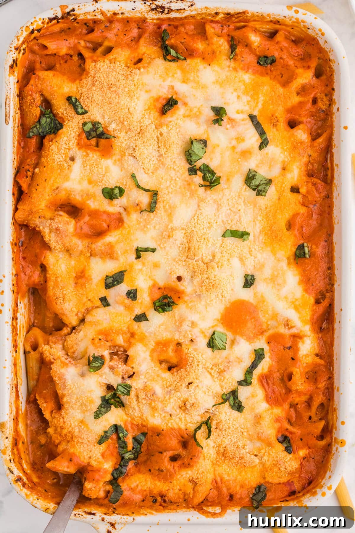 One-Dish Baked Penne 2 A perfectly baked No-Boil Baked Penne in a white casserole dish, garnished with fresh basil. The golden-brown, melted mozzarella and creamy ricotta create an inviting texture, promising a delicious, easy, and cheesy one-pan pasta dinner that requires no pre-boiling, ideal for a comforting family meal.