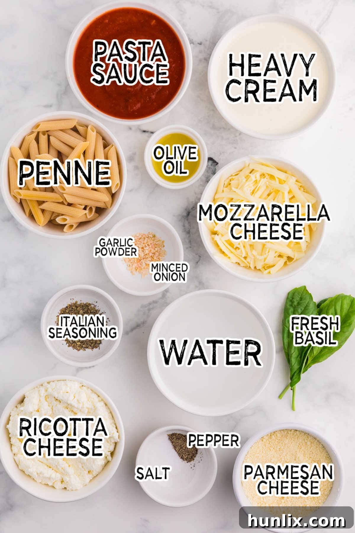 One-Dish Baked Penne 3 A collection of fresh and dried ingredients neatly arranged on a marble counter, including uncooked penne pasta, a jar of marinara sauce, heavy cream, various cheeses, and spices, all ready to be transformed into a delicious No-Boil Baked Penne.