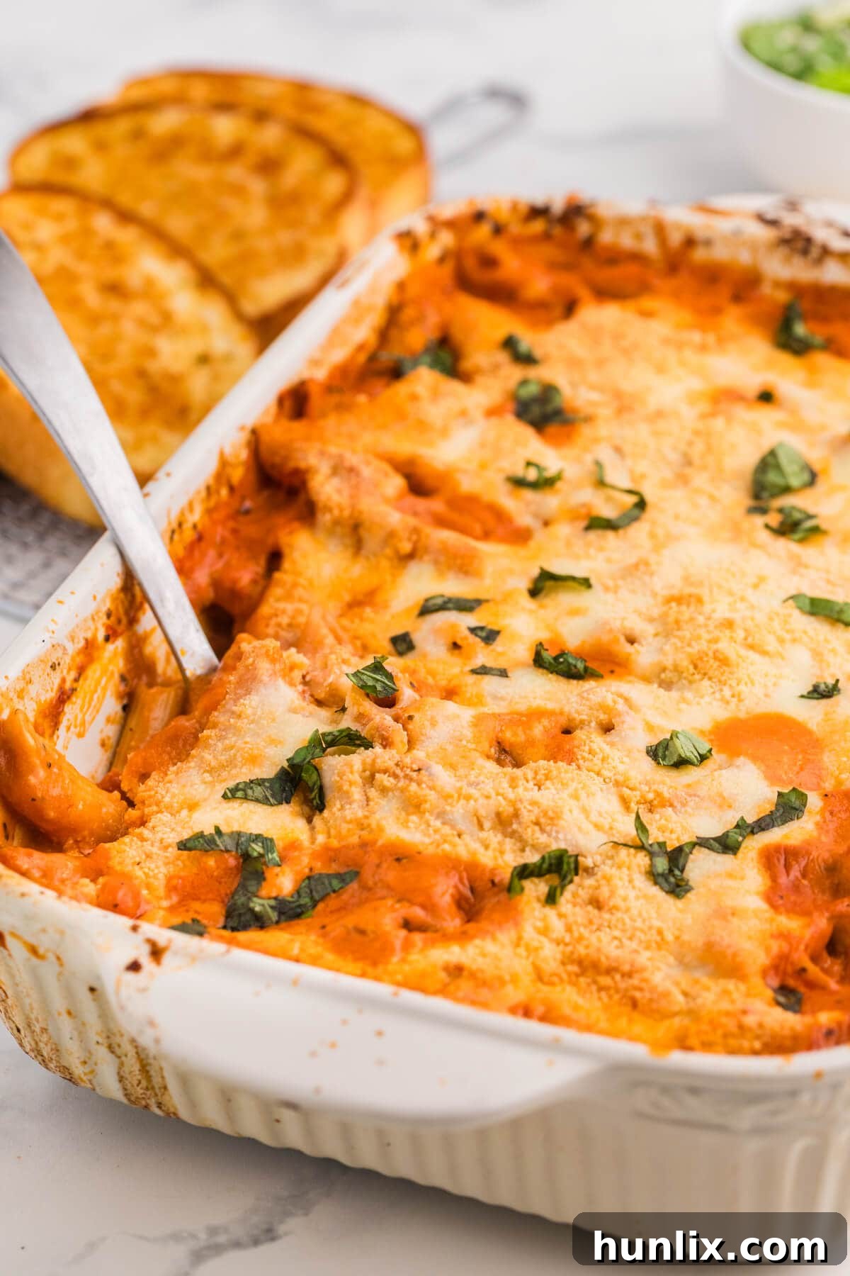 One-Dish Baked Penne 6 No-Boil Baked Penne in a large casserole dish, with a serving spoon lifting a portion, showcasing the melted cheese and rich sauce, ready to be served. This image captures the essence of a comforting, easy, and cheesy one-pan pasta dinner perfect for family meals.