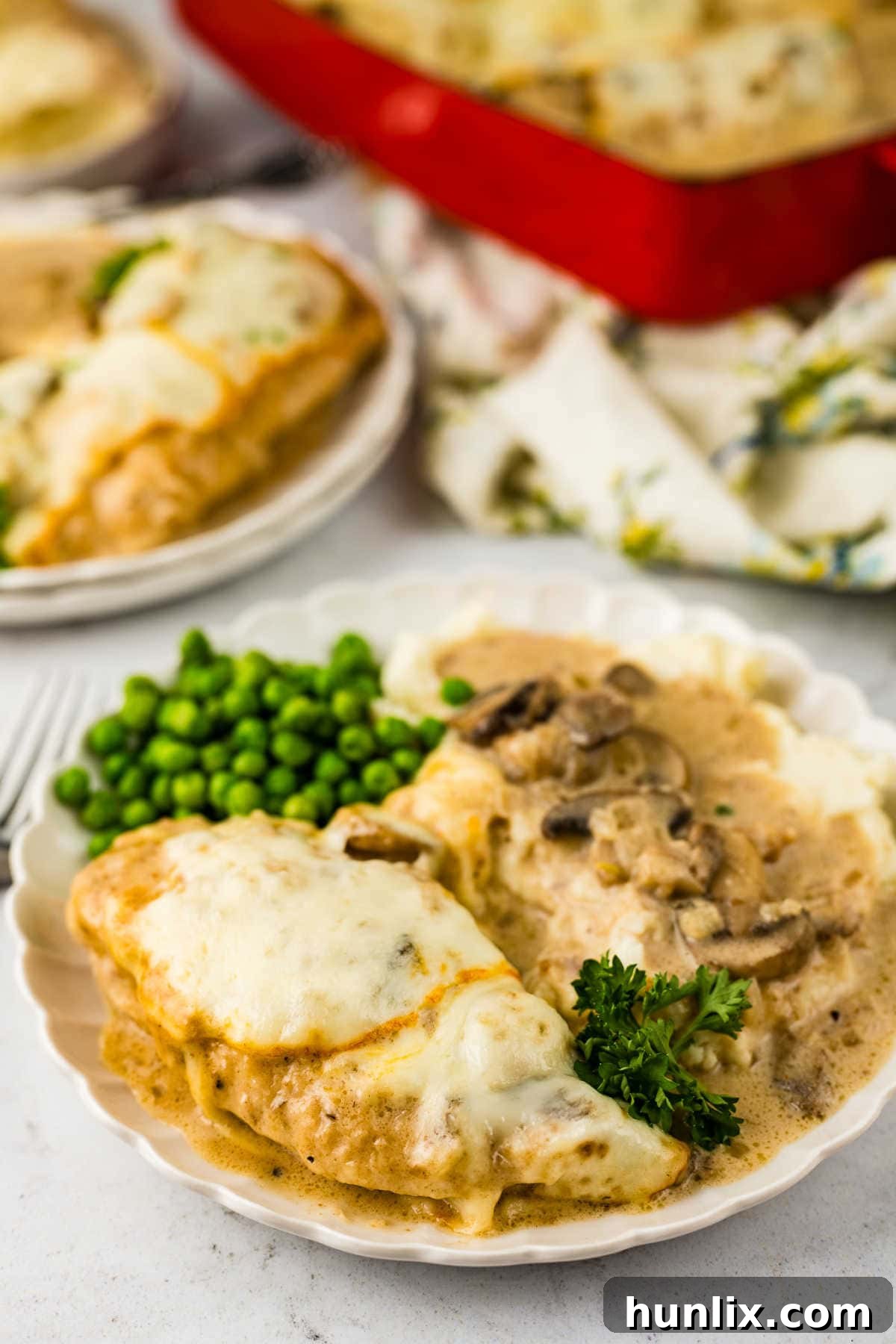 Chicken Gloria served on a plate with mashed potatoes and green peas.