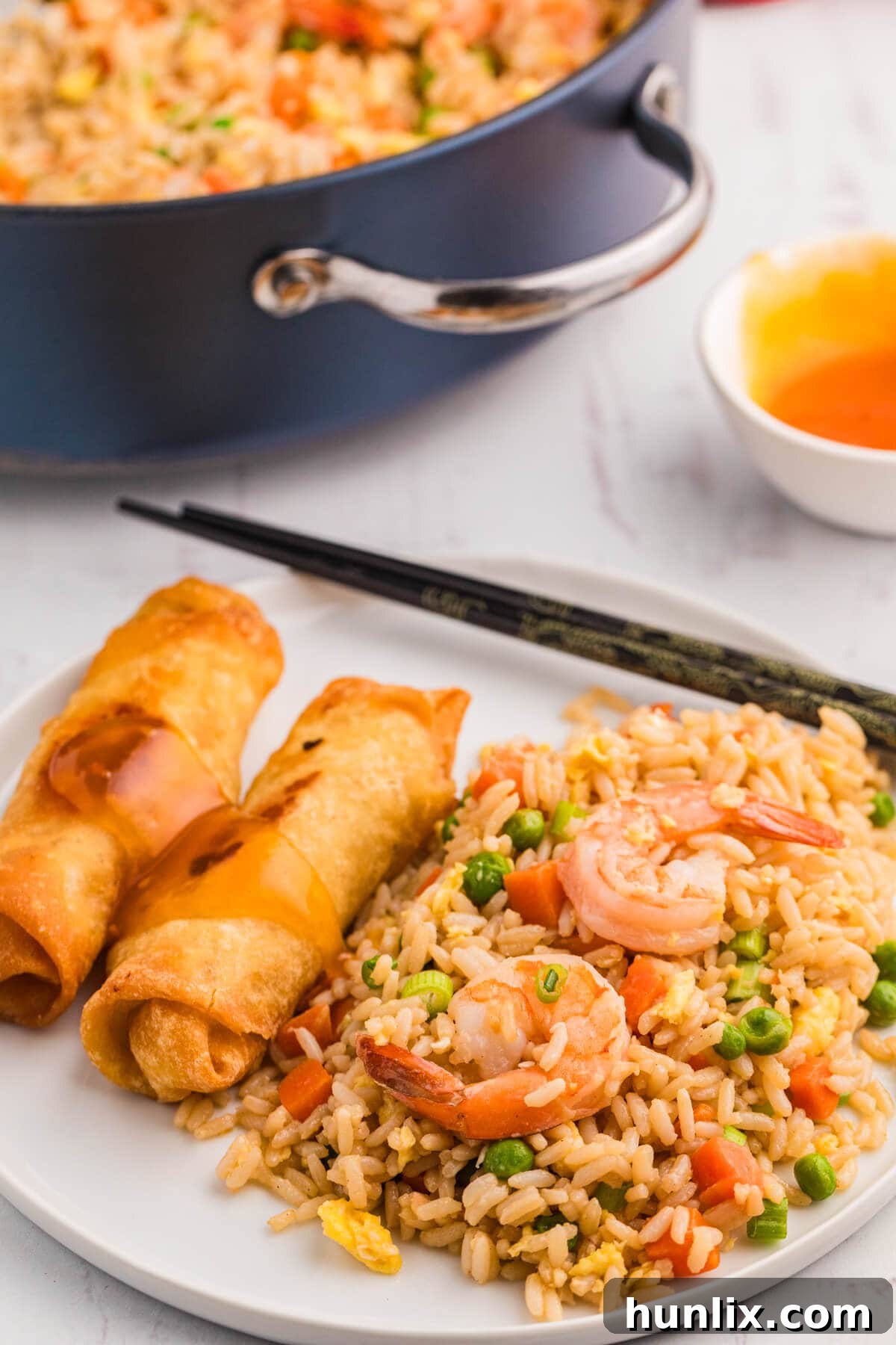 A plate of homemade shrimp fried rice, garnished with green onions and served alongside spring rolls, creating a complete meal.
