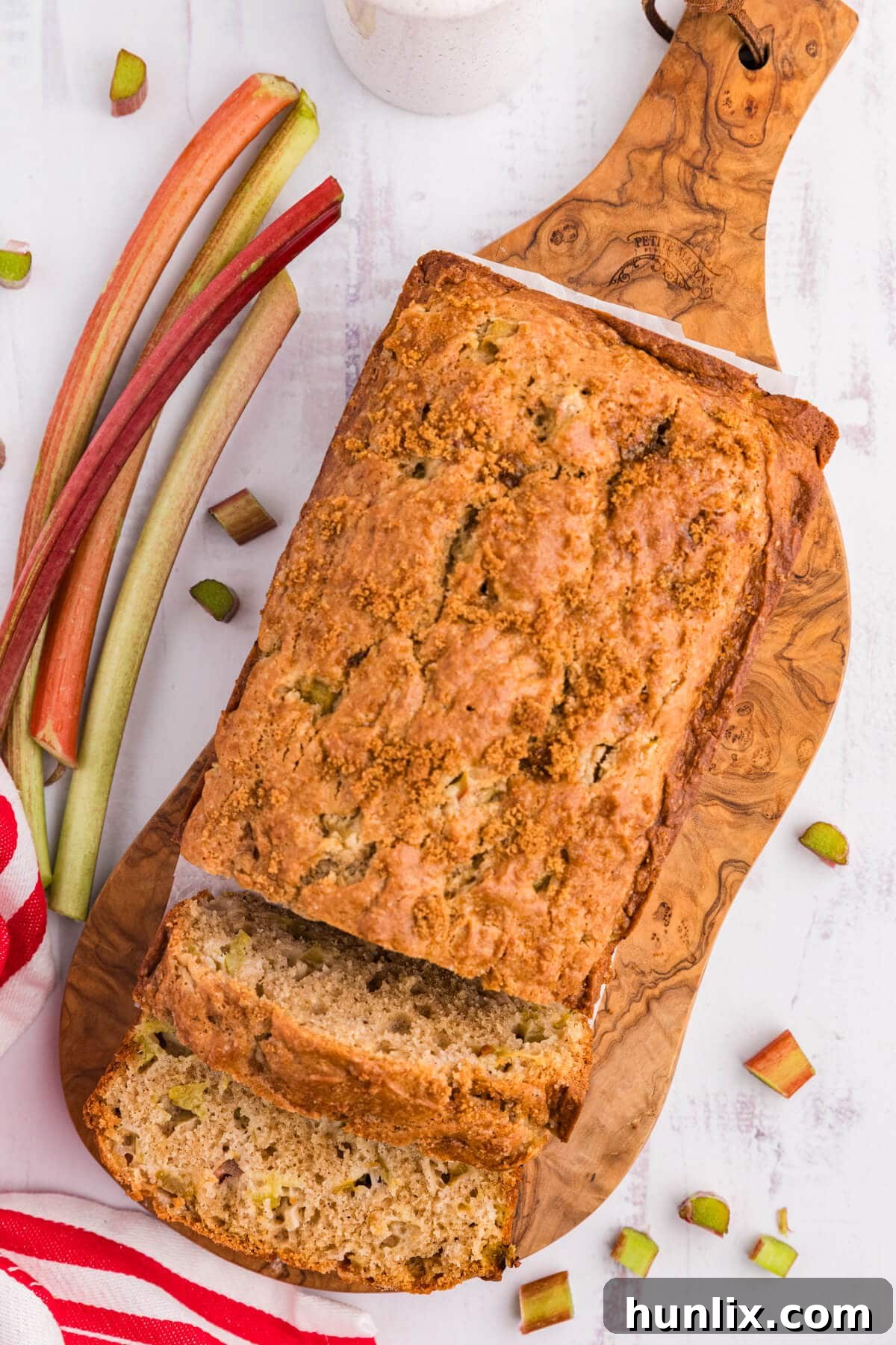 Tangy Rhubarb Loaf 7 A loaf of rhubarb bread on a wooden surface with slices already cut off and some crumbs.