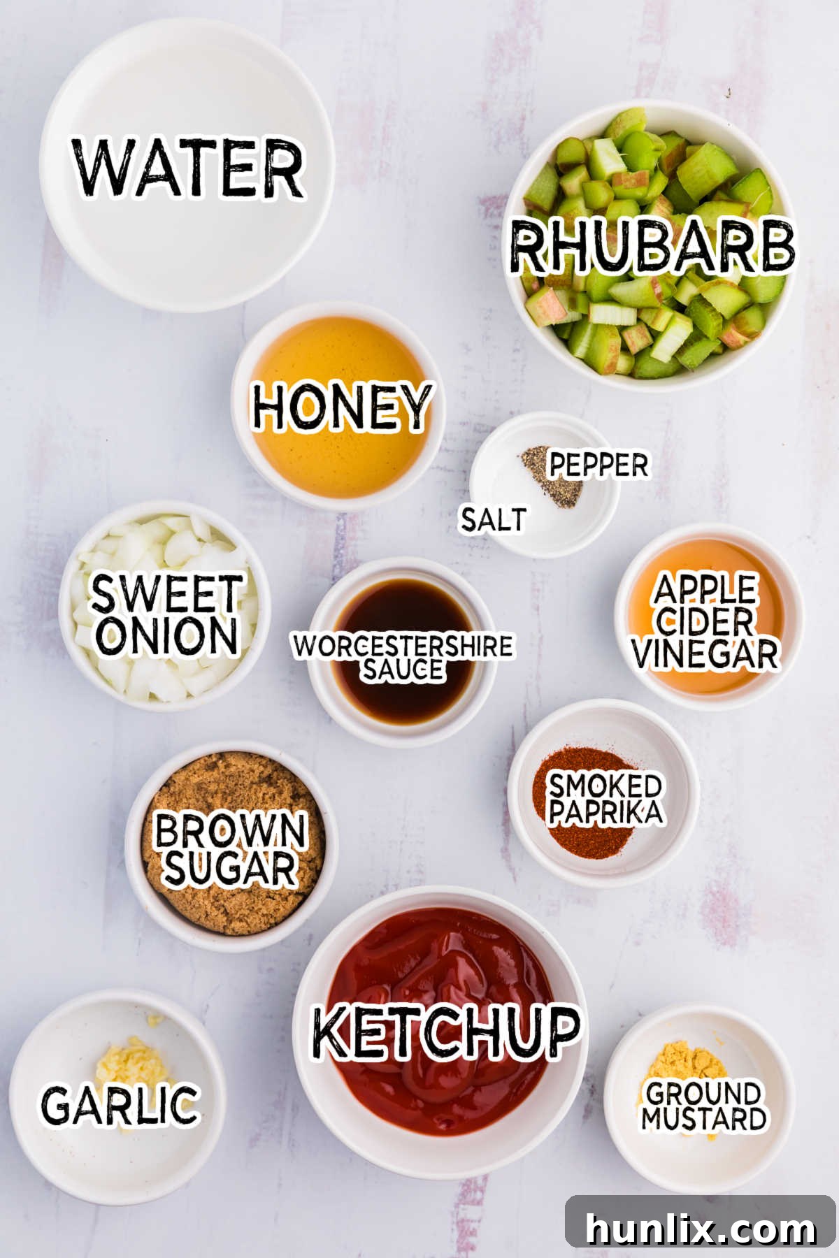 A collection of fresh ingredients for Rhubarb BBQ Sauce, including chopped rhubarb, onion, garlic, and various spices, neatly arranged on a white wooden background.