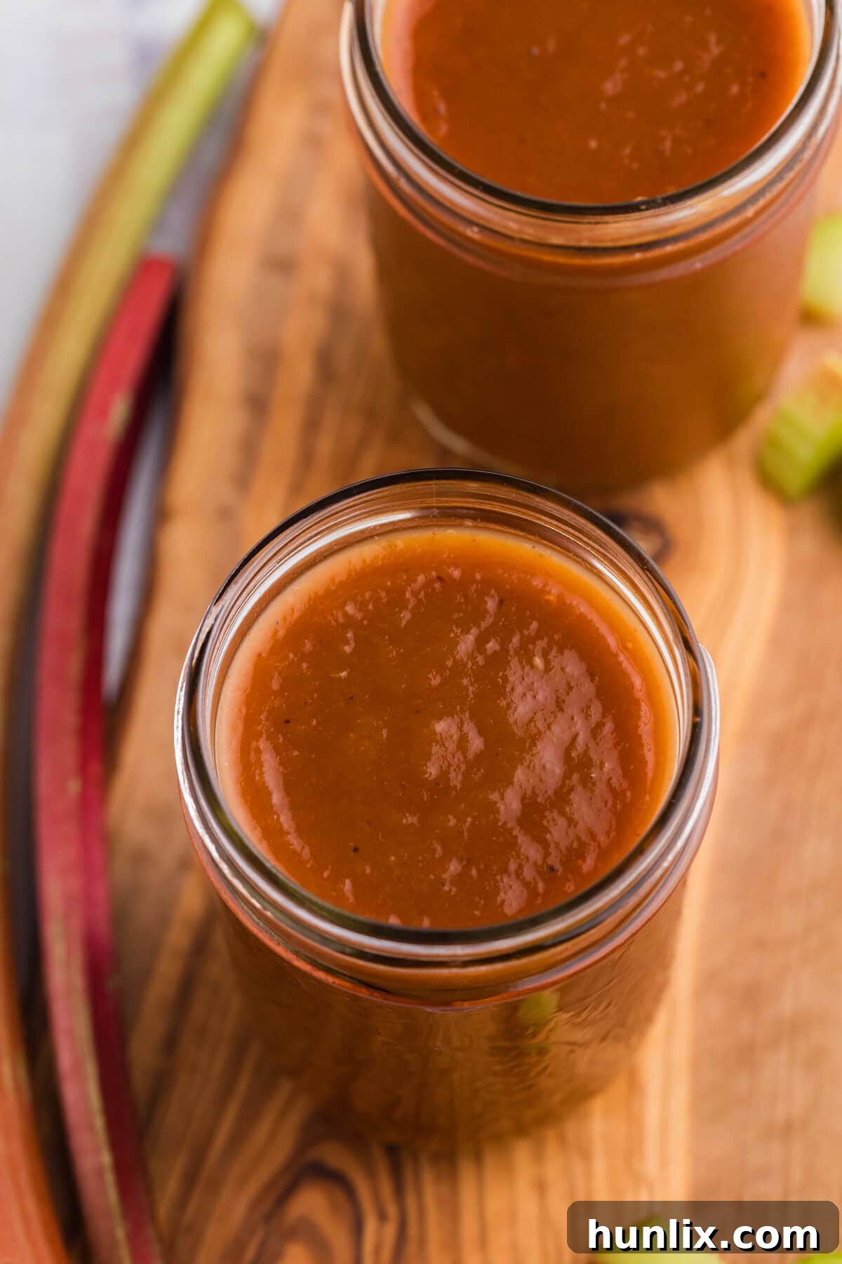 Multiple glass jars filled with Rhubarb BBQ Sauce, arranged on a wooden cutting board, showcasing the vibrant color and readiness for storage or gifting.
