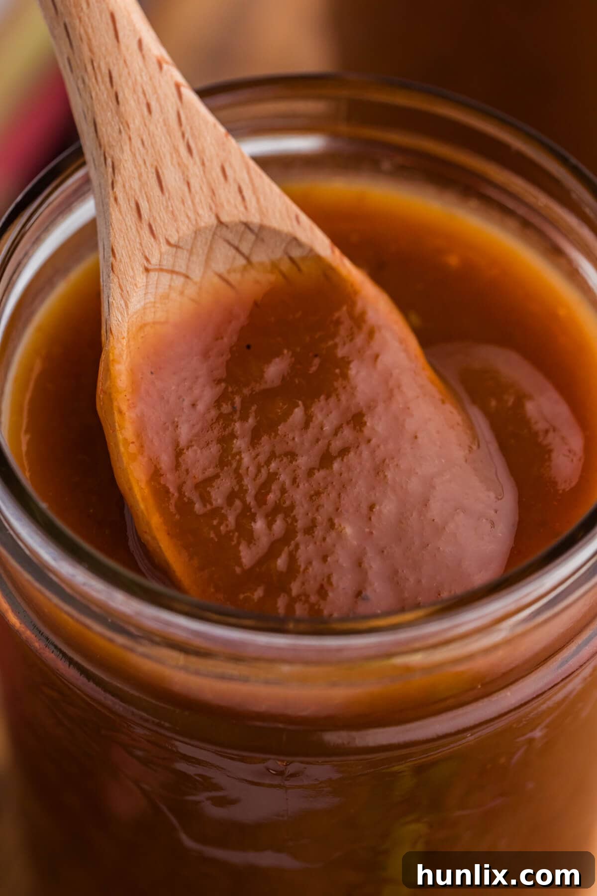 A wooden spoon scooping a generous portion of Rhubarb BBQ Sauce from a glass jar, highlighting its thick and luscious texture.