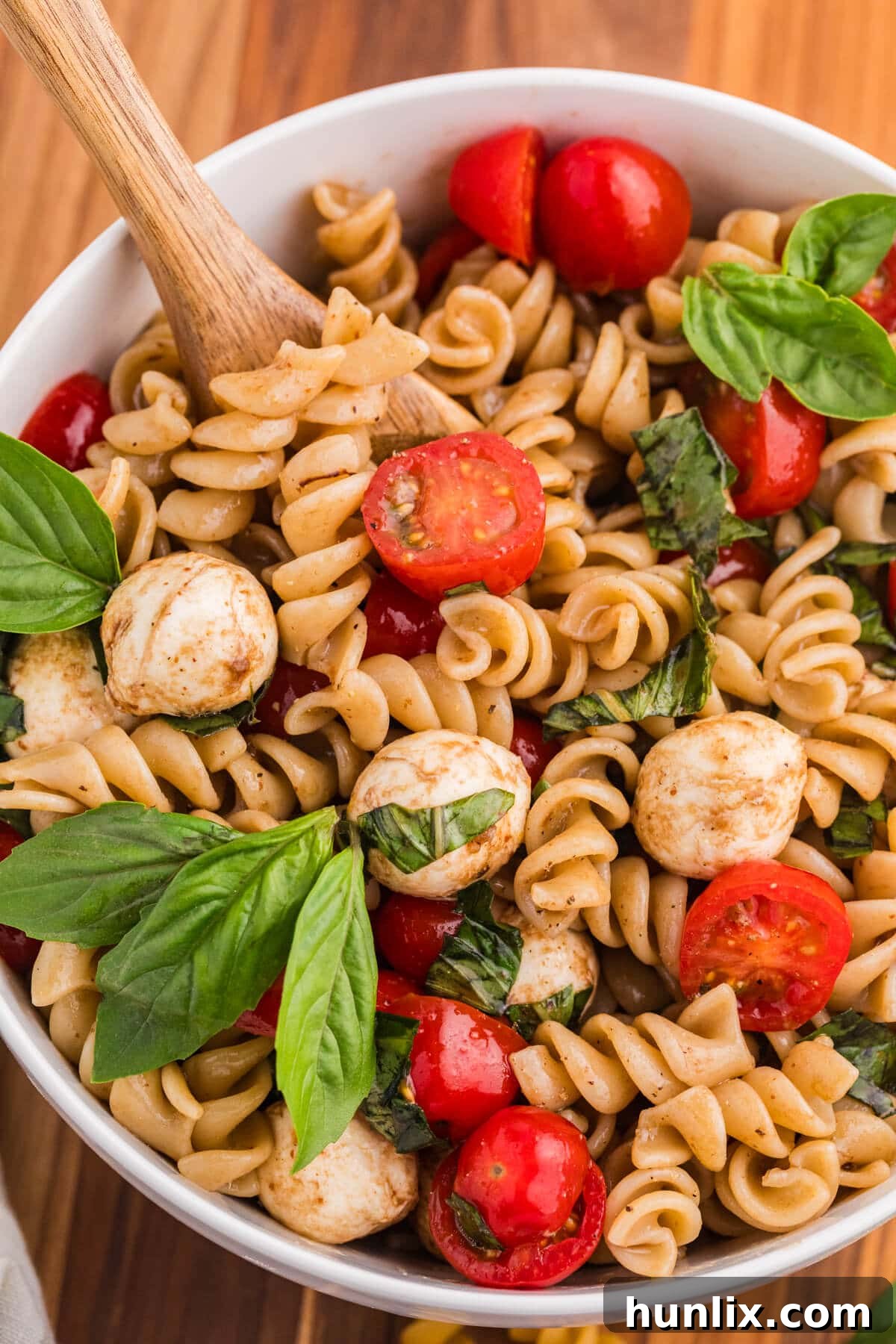 A bowl of Caprese Pasta Salad with a wooden serving spoon, ready to be enjoyed.
