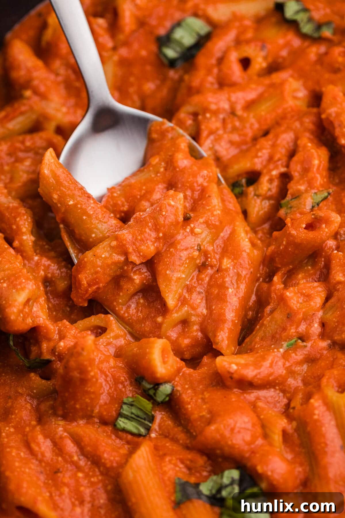 A close-up shot of creamy tomato pasta being served on a white spoon, showcasing its rich texture and perfect sauciness.