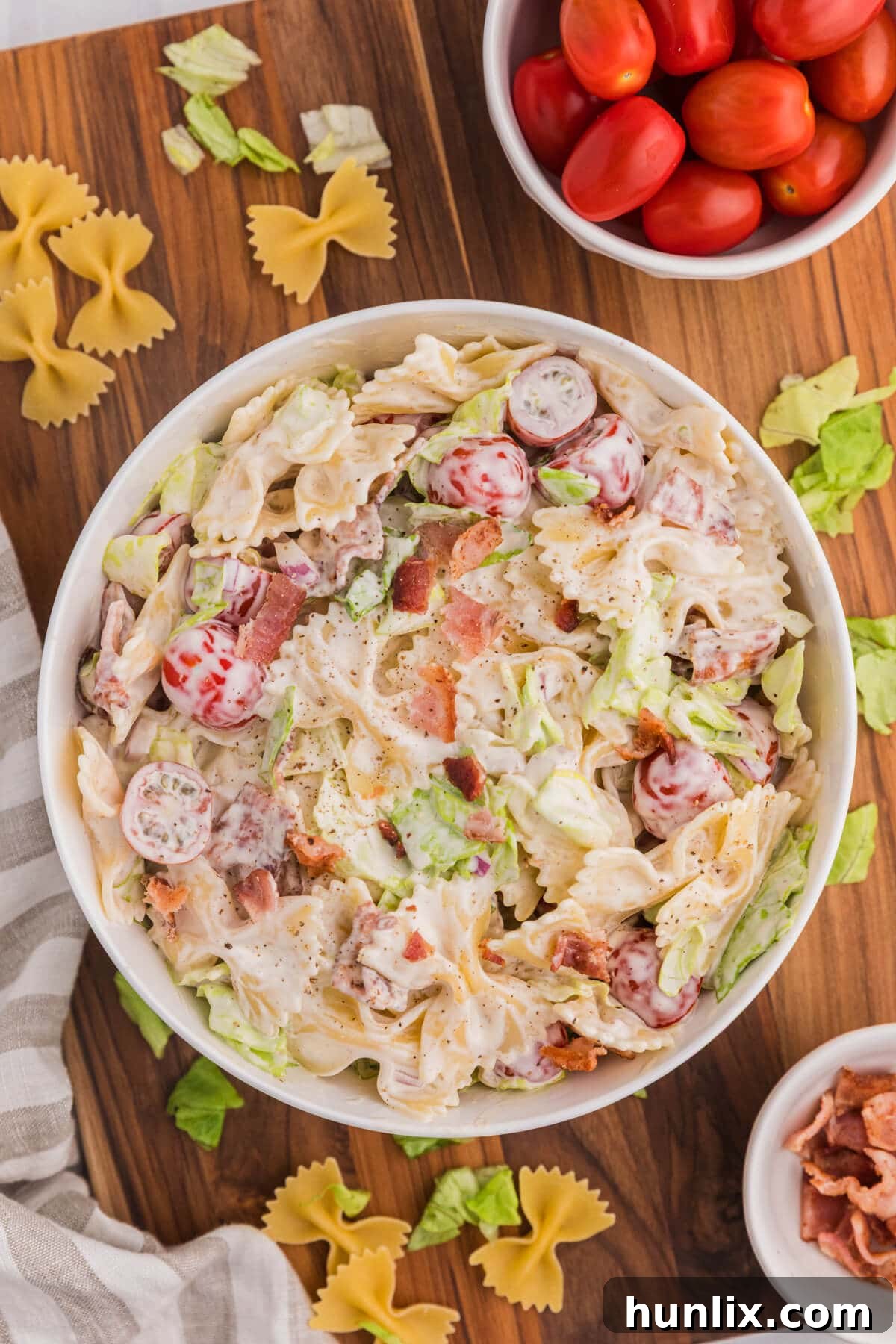 A bowl of BLT Pasta Salad on a wooden cutting board, garnished with fresh herbs.