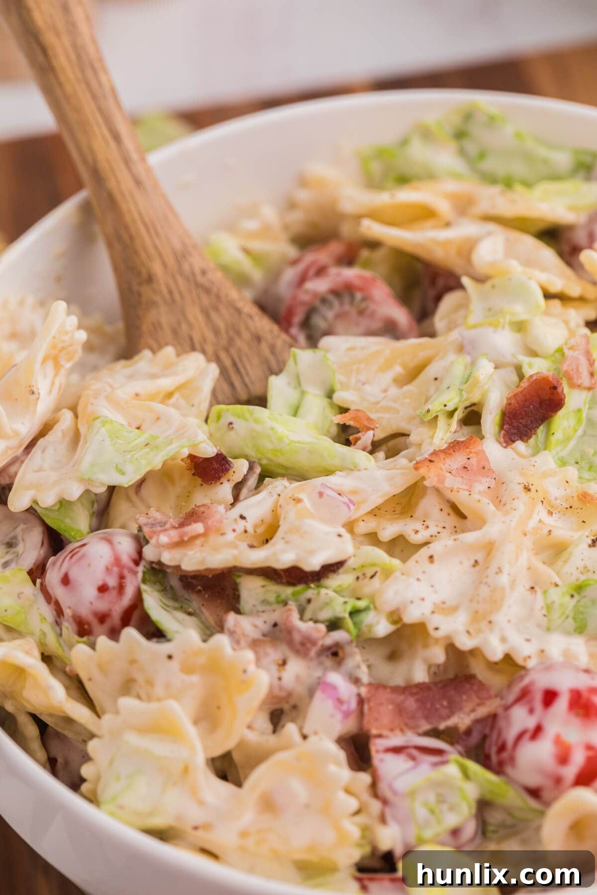The BLT pasta salad in a bowl with a wooden serving spoon, ready to be served.