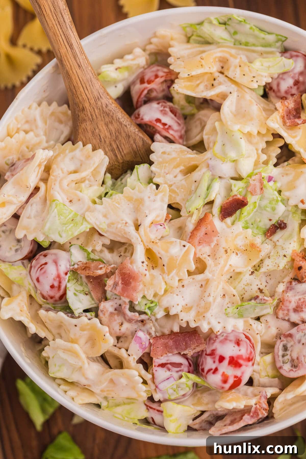 The BLT pasta salad in a bowl with a wooden serving spoon, close-up shot.