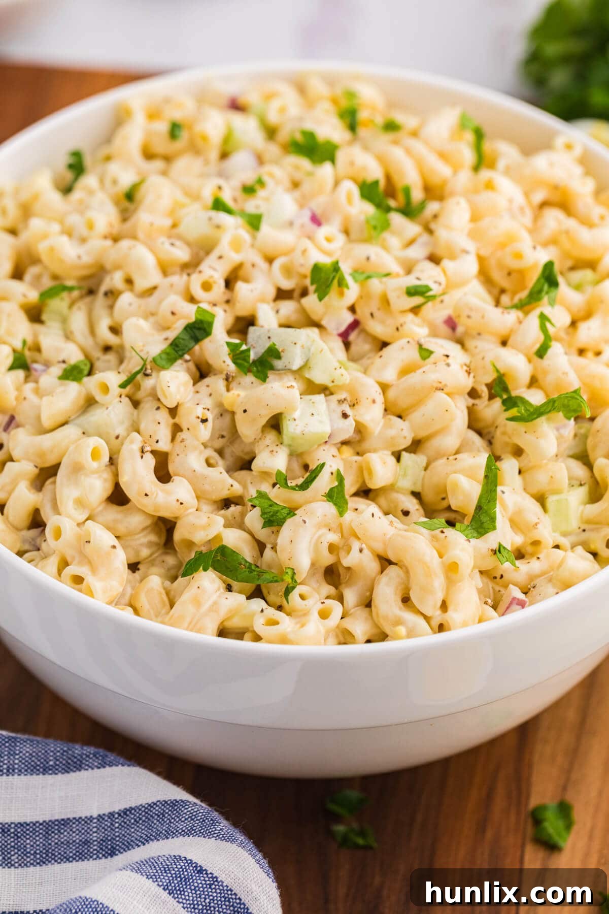 The classic creamy macaroni salad served in a elegant white bowl on a textured background.