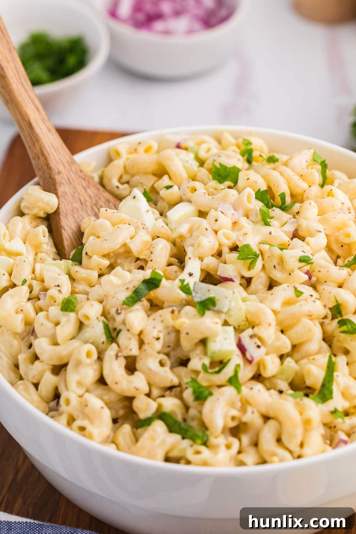 The classic creamy macaroni salad in a bowl with a wooden spoon, showcasing its rich texture and colorful ingredients.